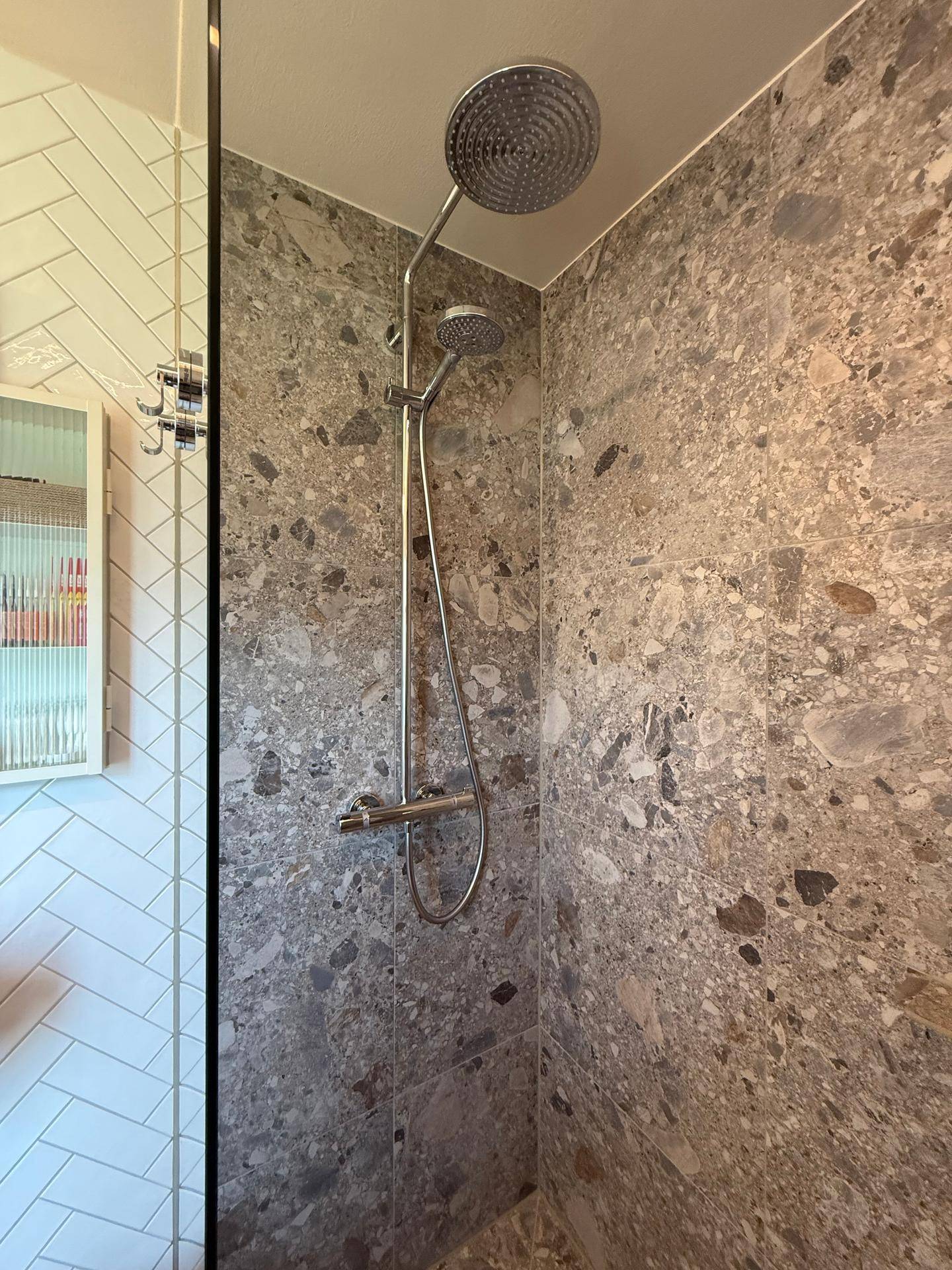 Detailansicht einer modernen Regendusche mit großformatigen Steinfliesen an der Wand.