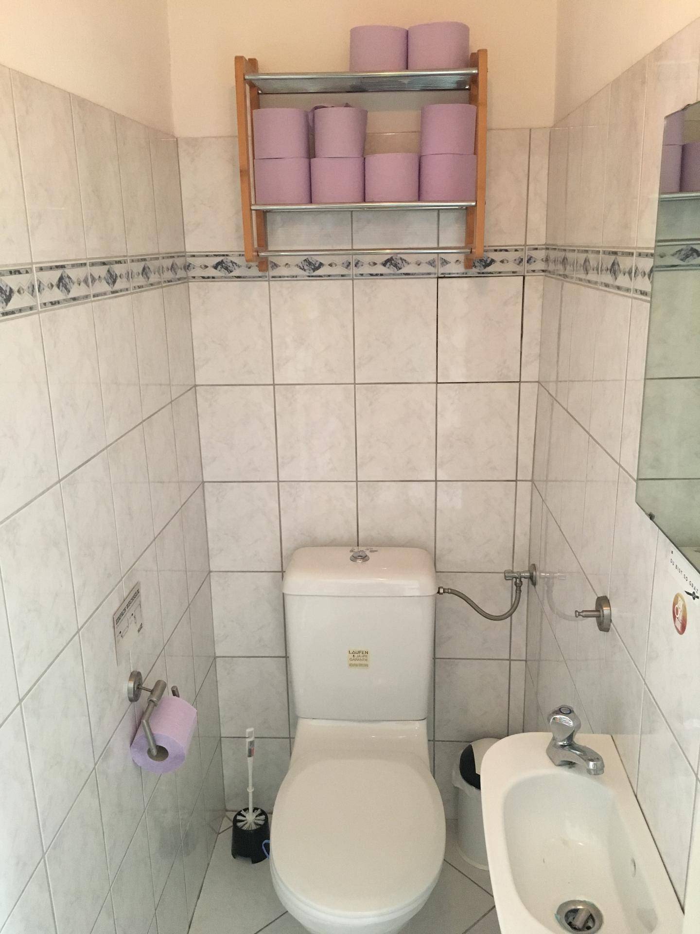 Funktionales WC mit Bidet, weißen Wandfliesen und einem Regal für Toilettenpapier.