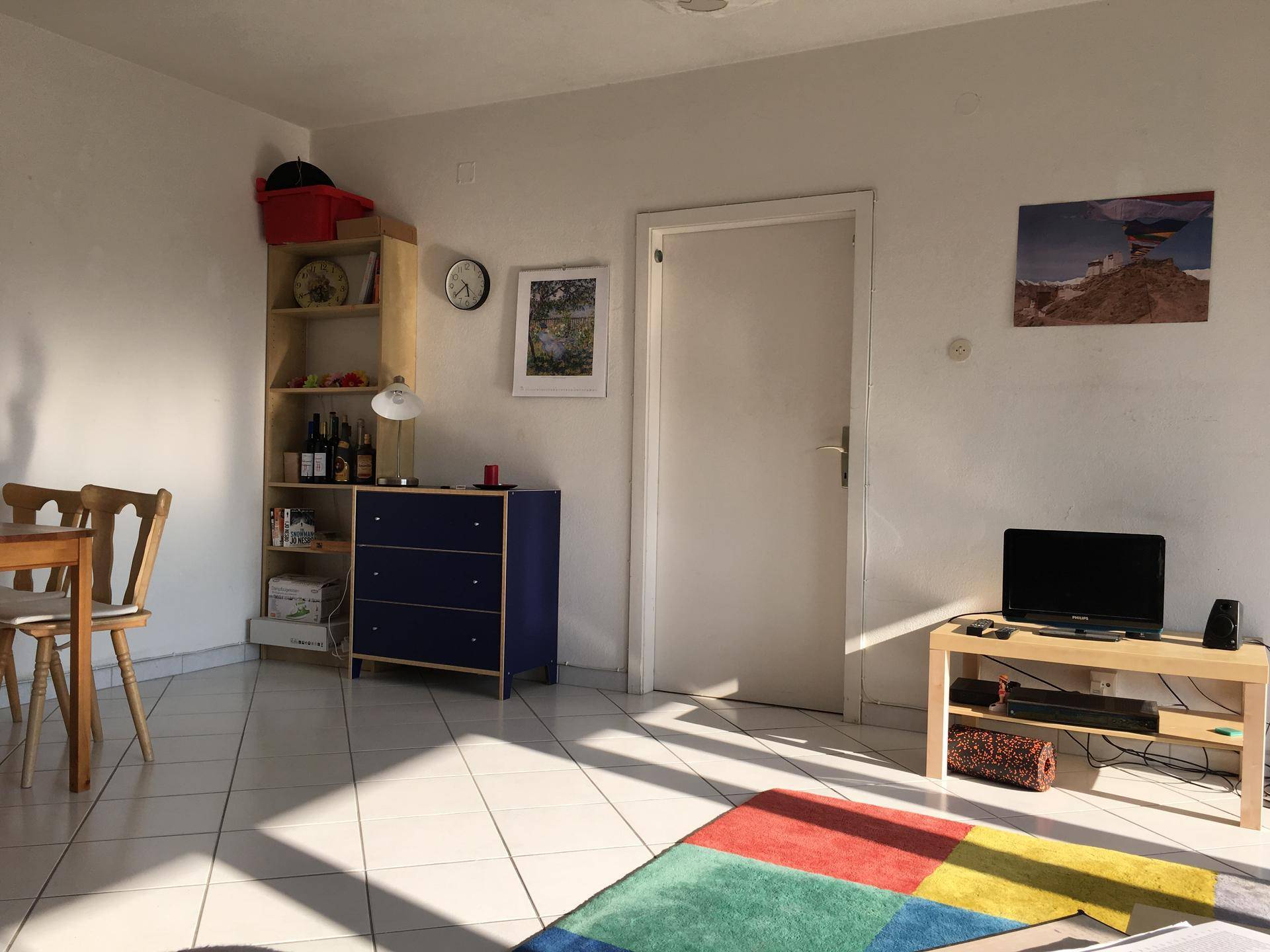 Helles Wohnzimmer mit Fliesenboden, farbenfrohem Teppich und Möbeln im warmen Sonnenlicht.