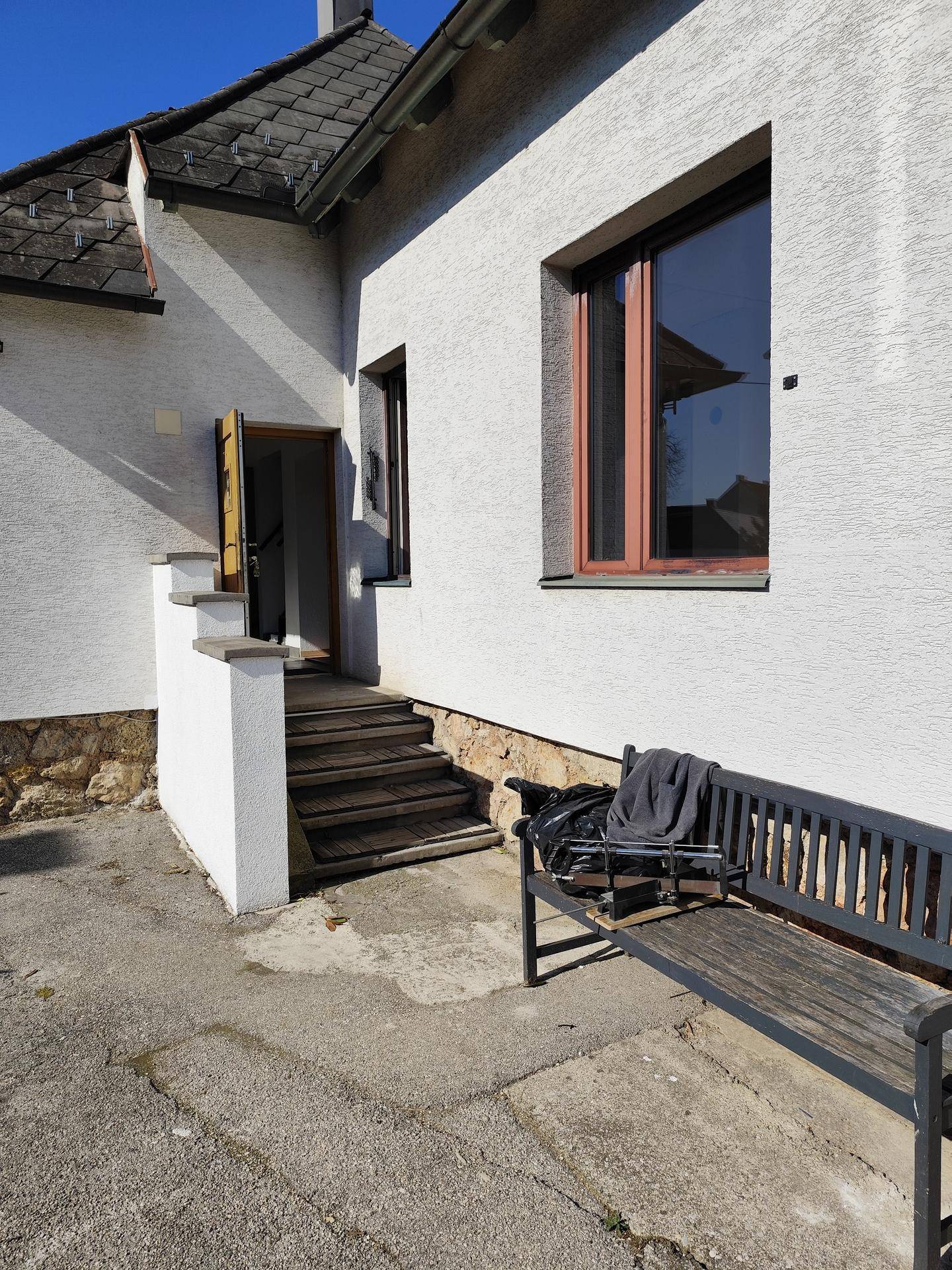 Seitlicher Eingangsbereich des Hauses mit Treppe und einer Holzbank im Freien.