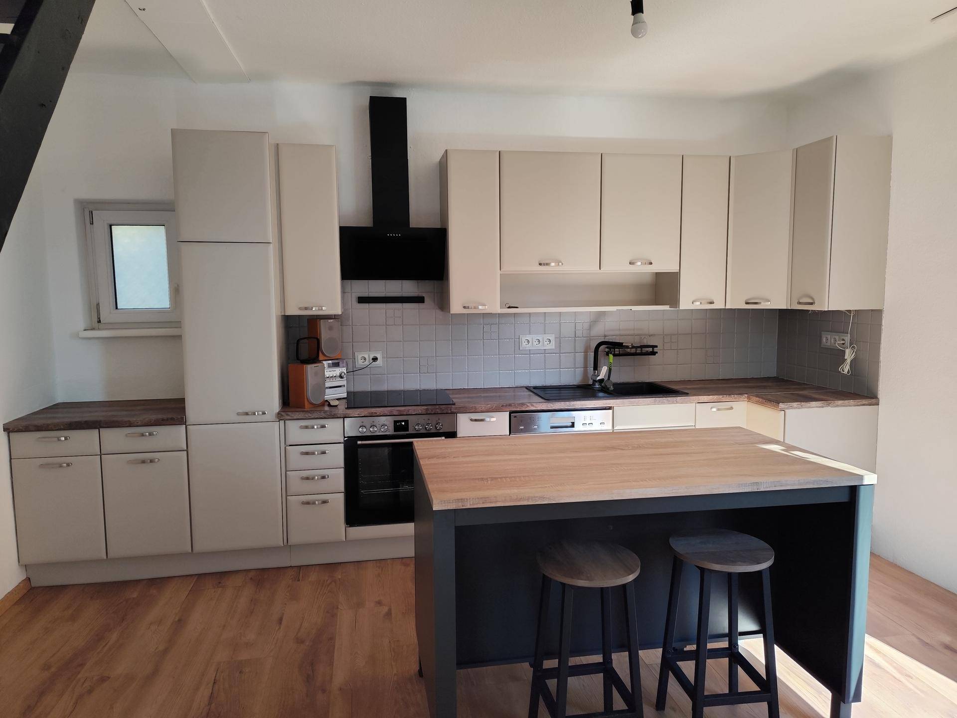 Moderne Einbauküche mit Kücheninsel, hellen Schränken und integrierten Geräten, bereit zum Kochen.