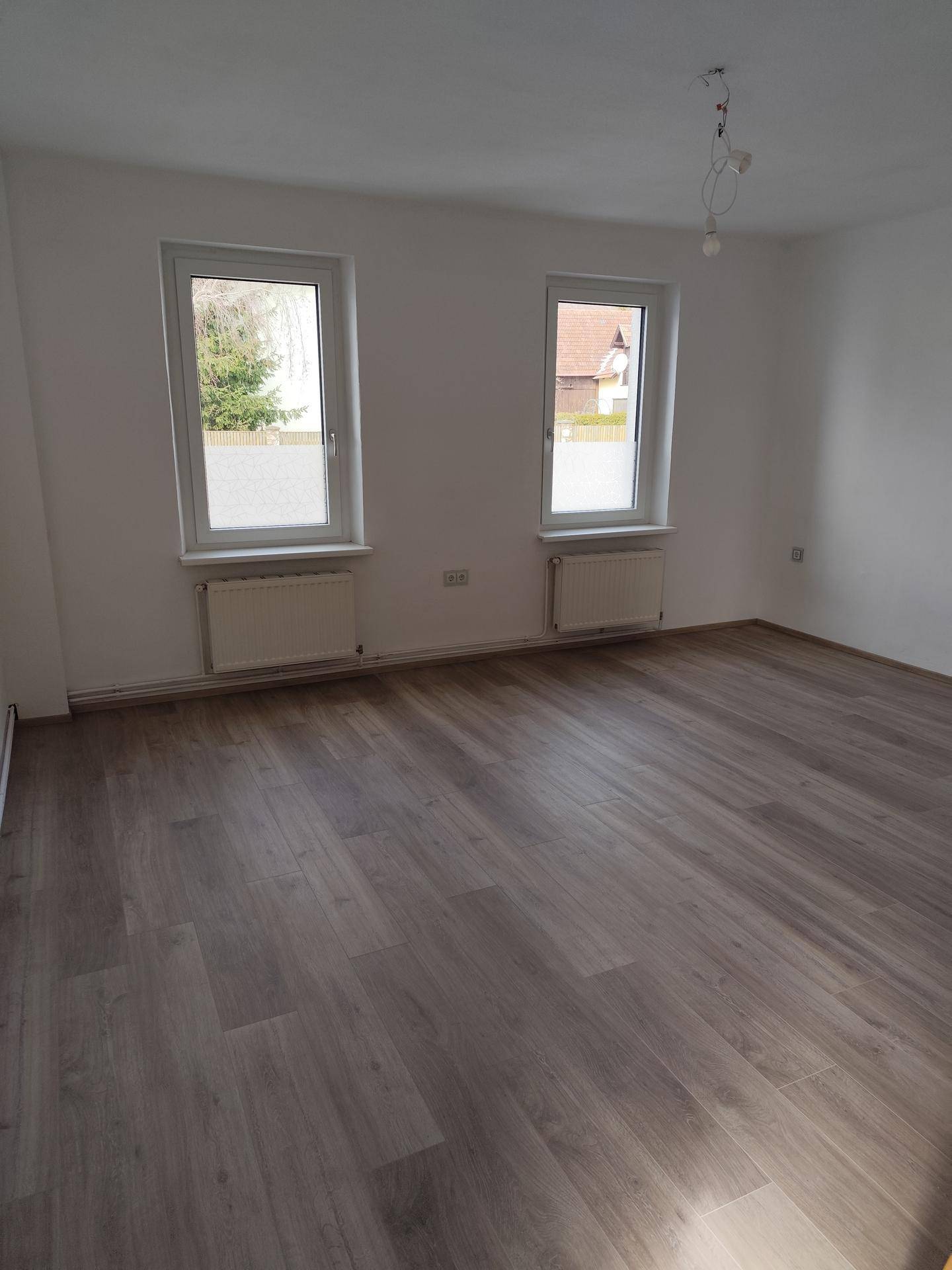 Geräumiger, heller Raum mit Laminatboden und zwei Fenstern, bereit zur individuellen Gestaltung.