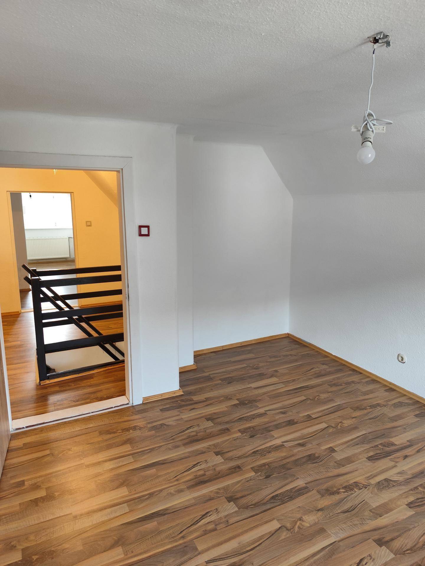 Heller Raum mit Laminatboden und Dachschräge, mit Blick auf eine offene Treppe.