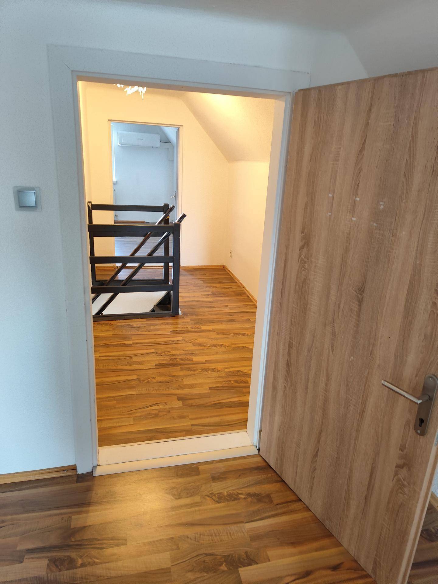 Heller Flur mit Laminatboden und Holztür, der zu weiteren Räumen und einer Treppe führt.