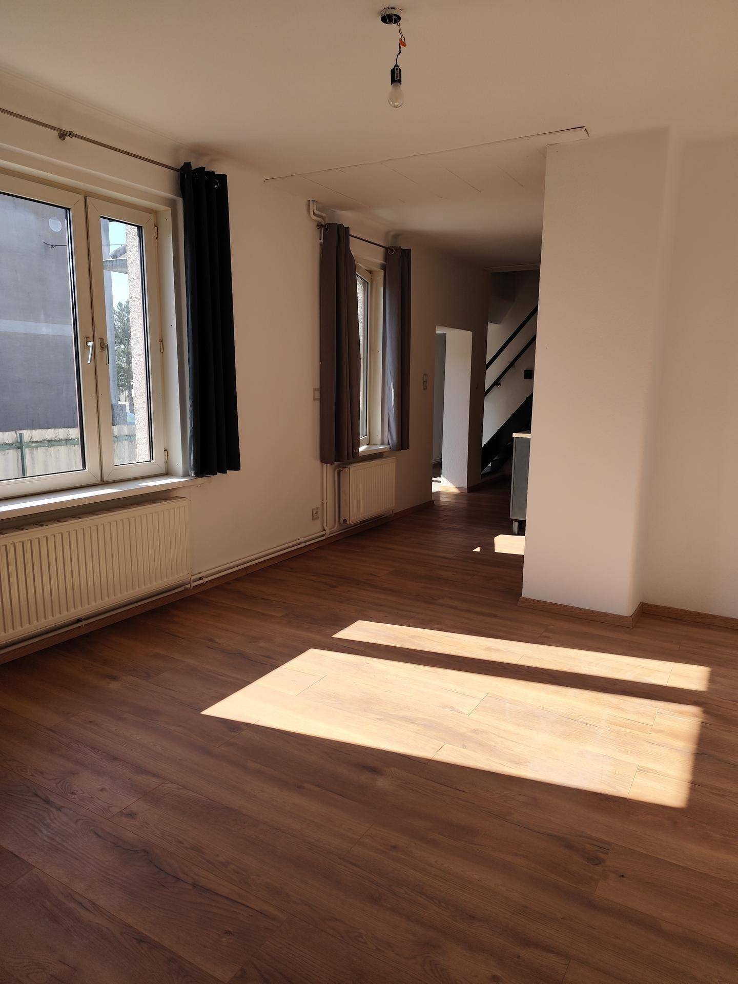 Heller Wohnbereich mit Laminatboden und Fenstern, die viel Tageslicht hereinlassen, mit Blick auf den Flur.