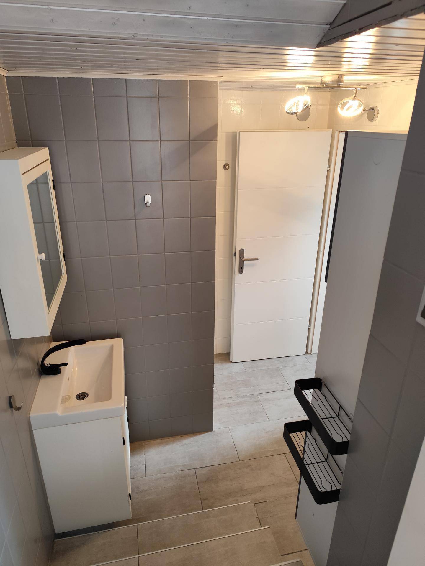 Modern gefliestes Badezimmer mit Einzelwaschbecken und Spiegelschrank, hell und funktional gestaltet.