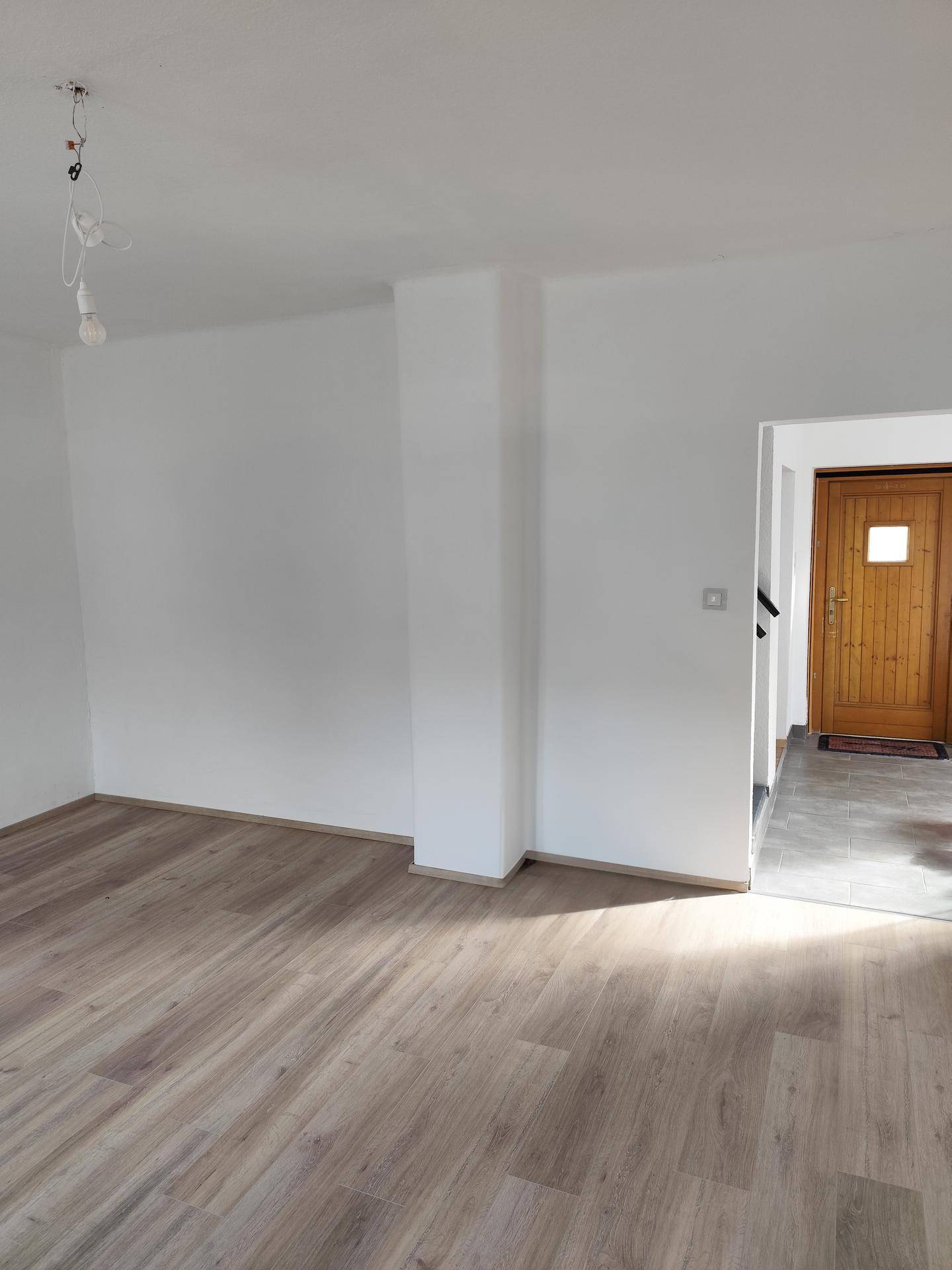 Heller Wohnbereich mit Laminatboden und Zugang zum Eingangsbereich, ideal für offene Gestaltung.