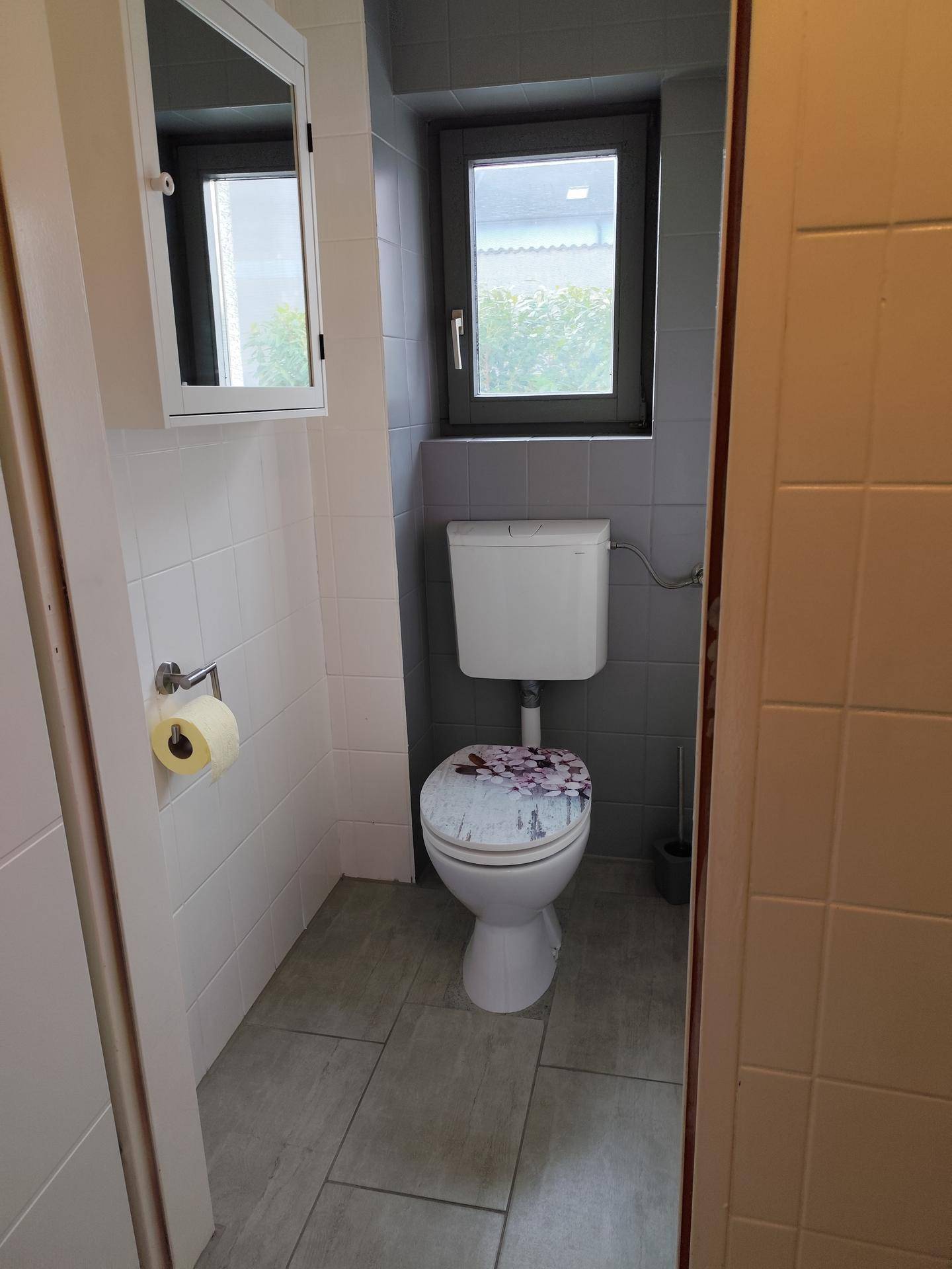 Helles WC mit Fenster, modern gefliest und mit einem Spiegelschrank ausgestattet.