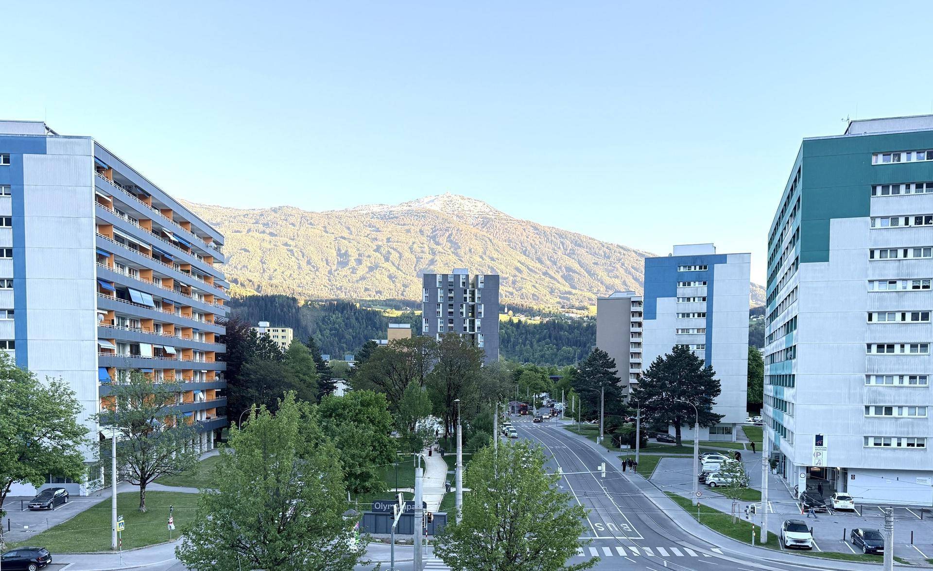 Weitläufiger Blick auf Wohngebäude, eine Straße und schneebedeckte Berge im Hintergrund.