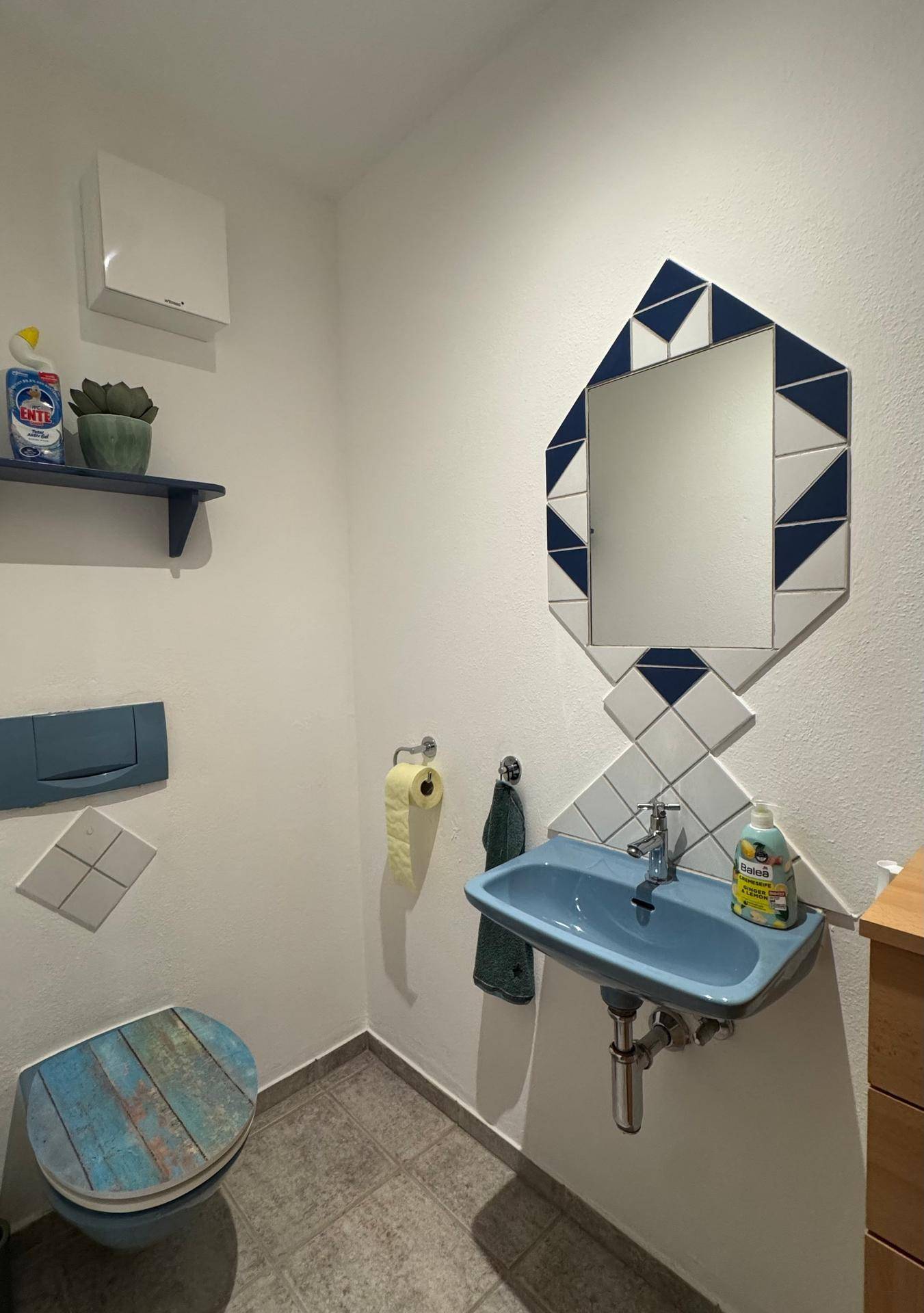Separates WC mit farbiger Toilette, kleinem Waschbecken und dekorativem Spiegel.