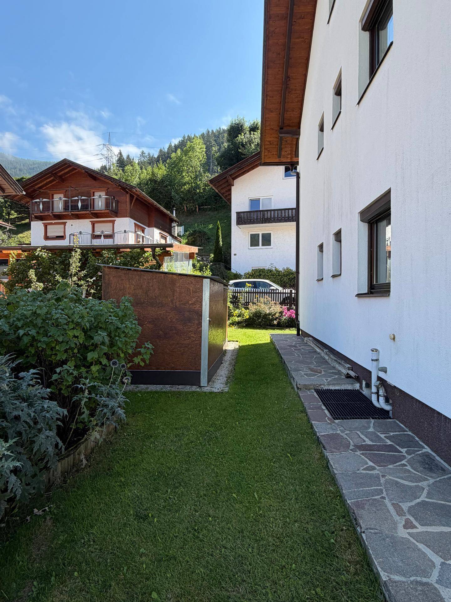 Seitlicher Gartenbereich mit Steinplattenweg und Blick auf die umliegende Berglandschaft.