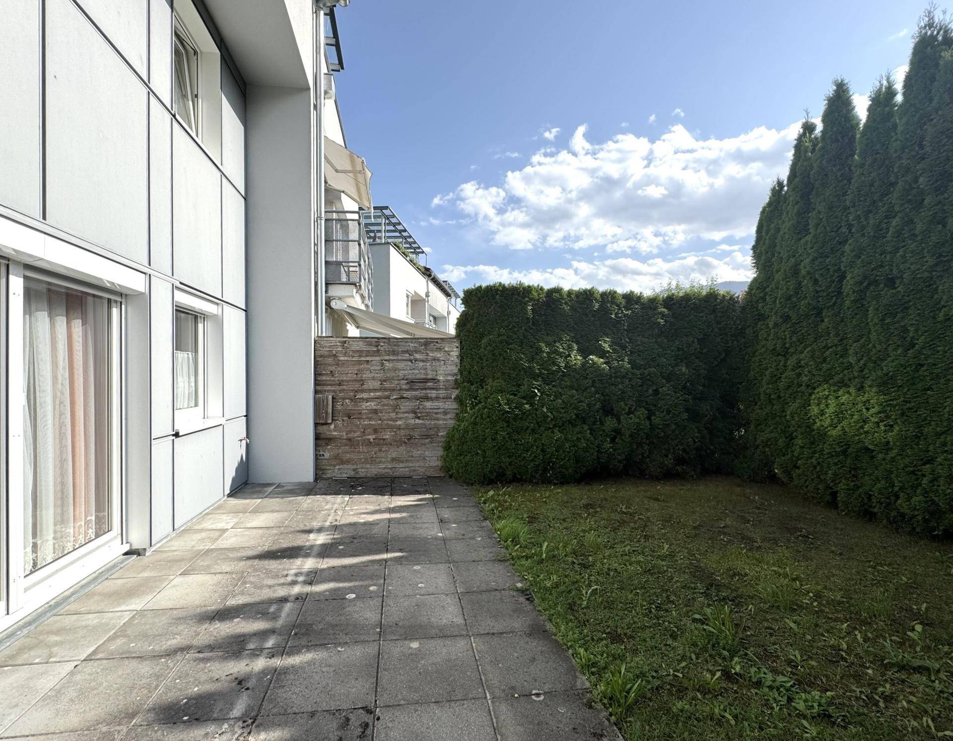 Außenbereich mit Terrasse und Rasenfläche, umgeben von hohen Hecken für mehr Privatsphäre.