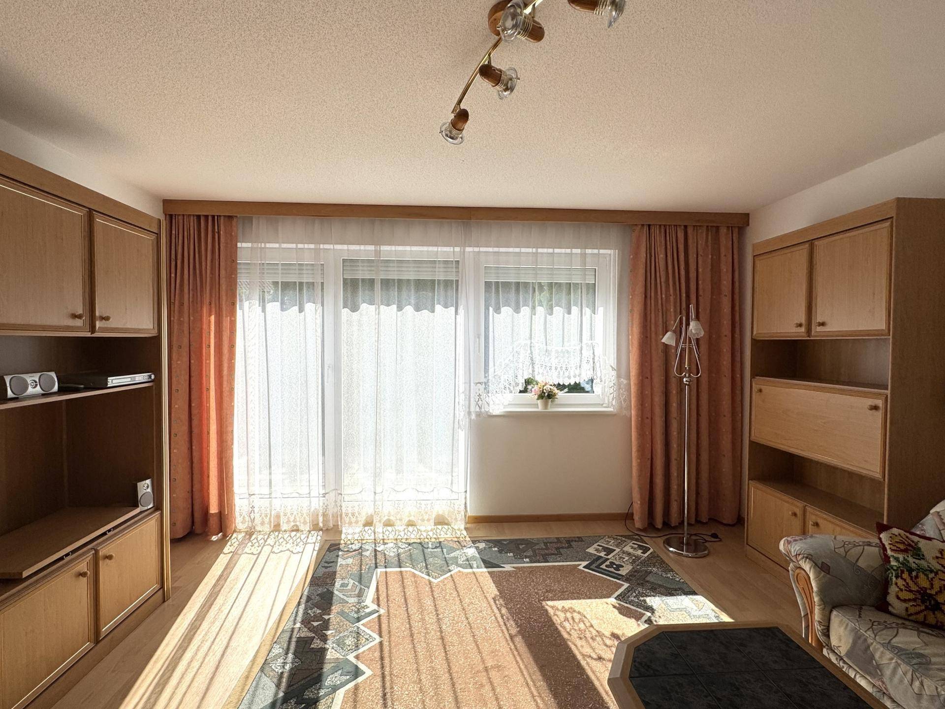 Wohnzimmer mit Laminatboden, großen Fenstern und traditionellen Möbeln, hell und sonnig.