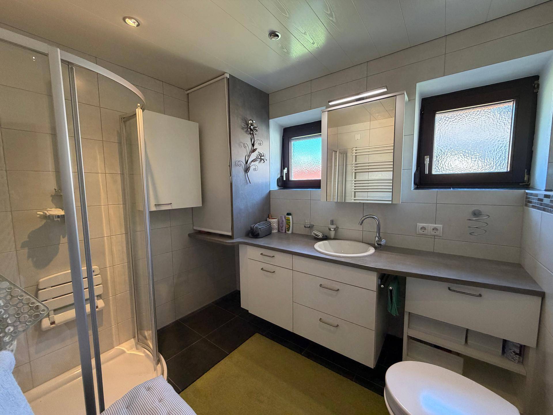Modernisiertes Badezimmer mit Duschkabine, Waschtisch und zwei Fenstern für Tageslicht.