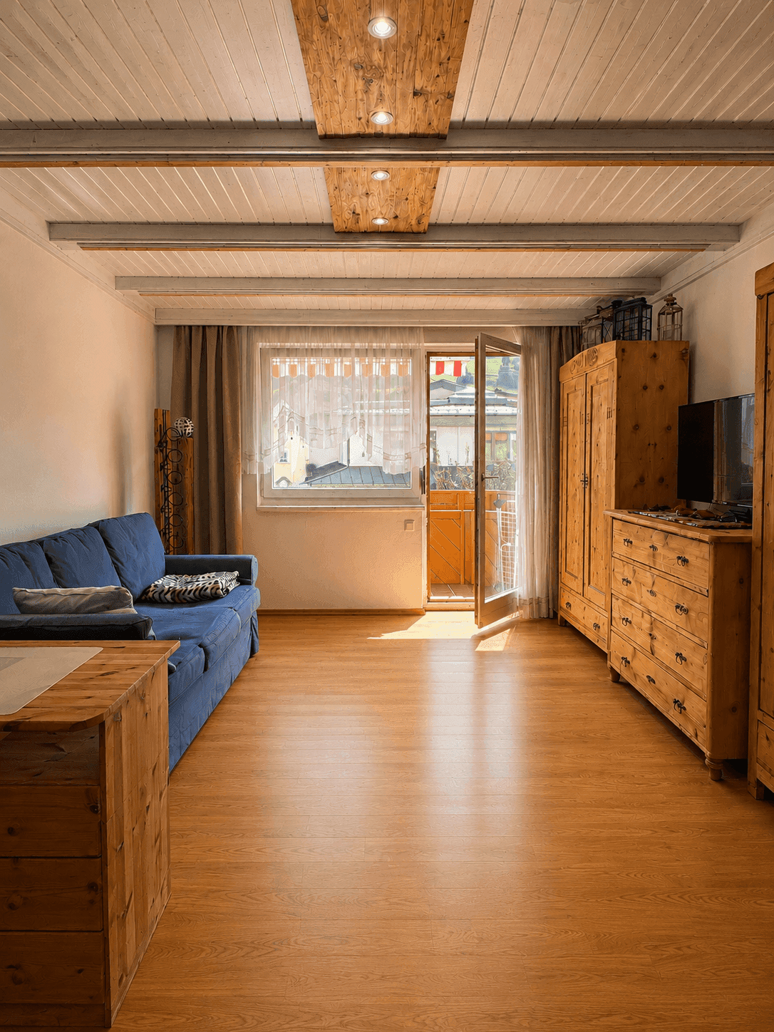 Helles Wohnzimmer mit blauem Sofa, rustikalen Holzmöbeln und Zugang zu einem Balkon.