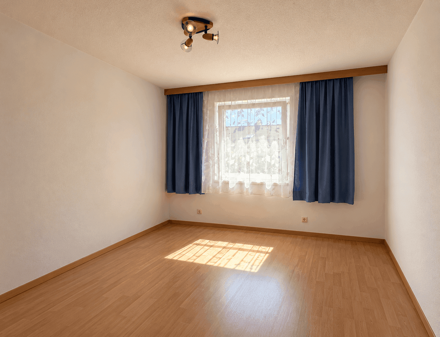 Helles Schlafzimmer mit Parkettboden und blauen Vorhängen, das eine angenehme Atmosphäre schafft.