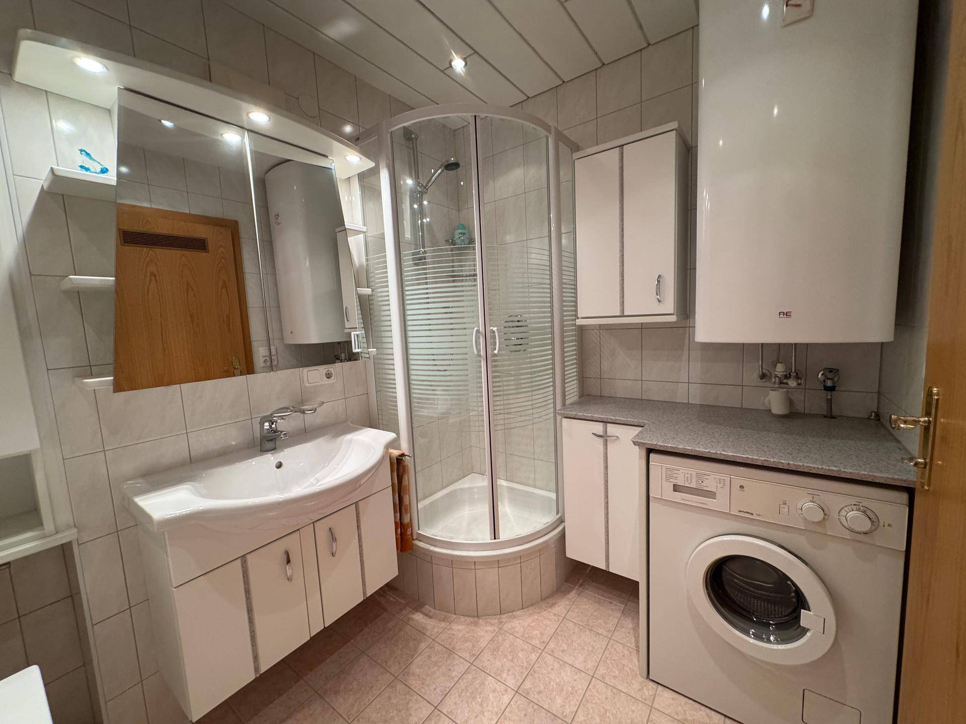 Badezimmer mit Duschkabine, Waschbecken, Spiegelschrank und Waschmaschine.