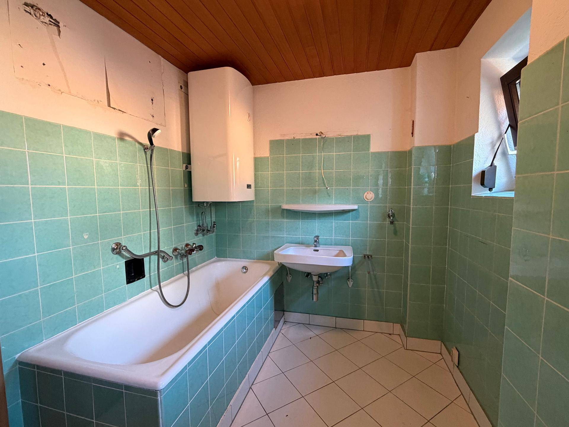 Badezimmer mit mintgrünen Fliesen, Badewanne und Waschbecken, im Stil der 80er Jahre.
