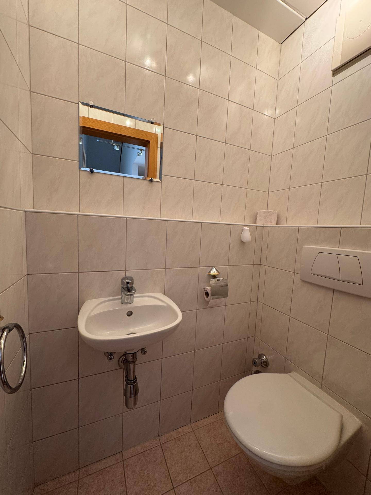 Kleines Gäste-WC mit Waschbecken, Toilette und hellen Fliesen an den Wänden.
