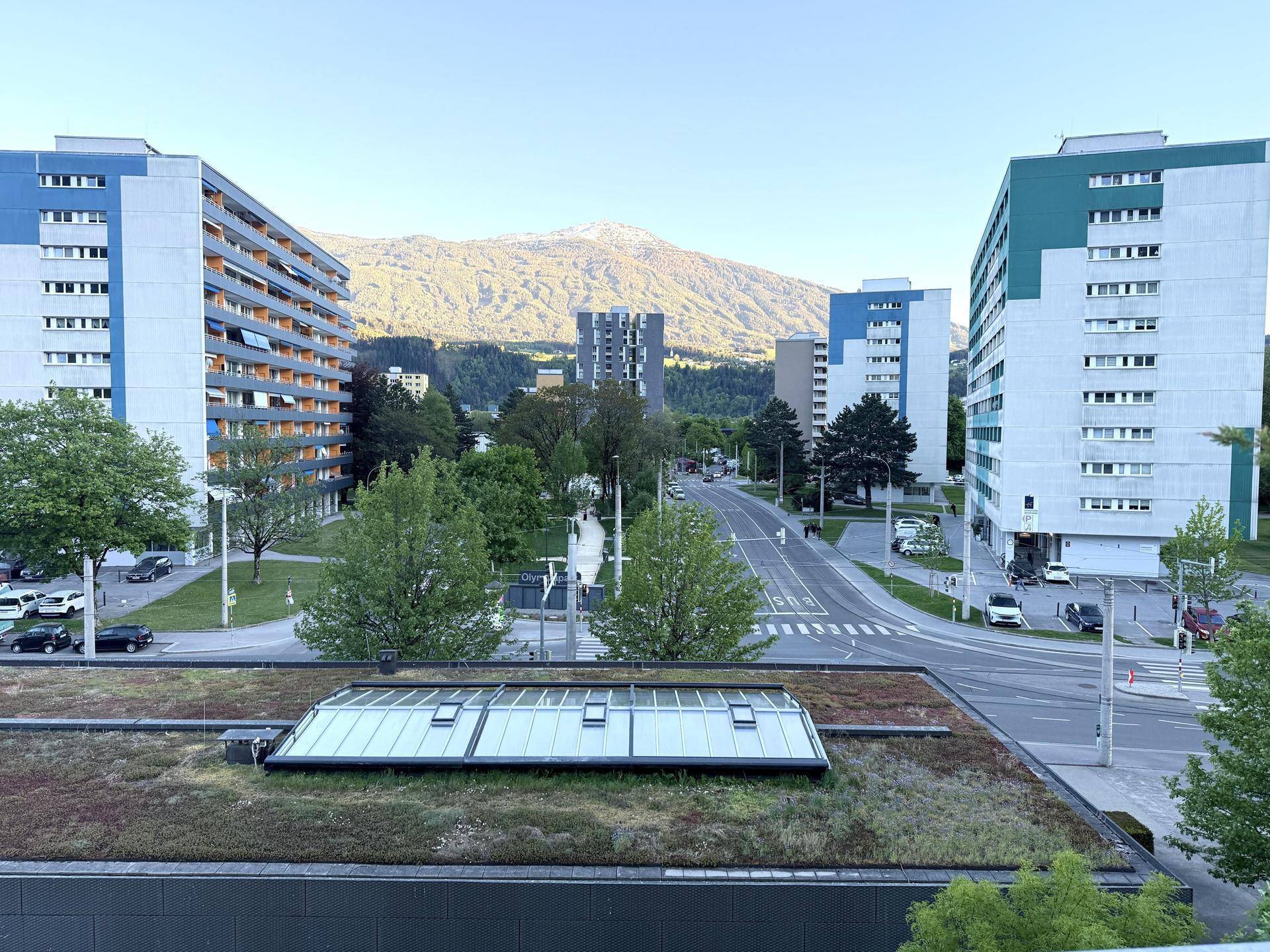 Blick auf moderne Wohngebäude, eine Straße und majestätische Berge im Hintergrund.