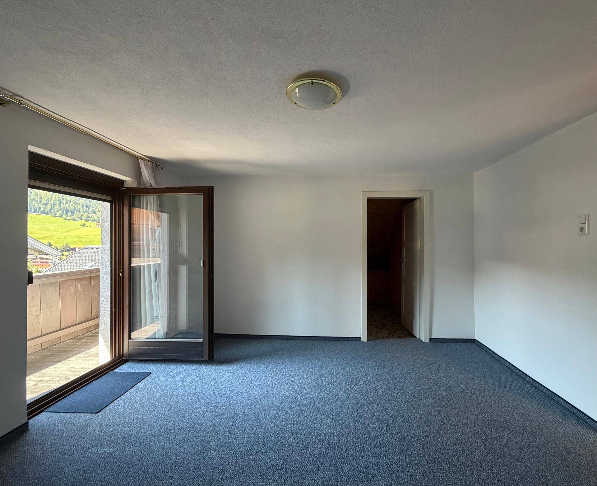 Heller Raum mit blauem Teppichboden und Zugang zu einem Balkon mit weitem Ausblick.