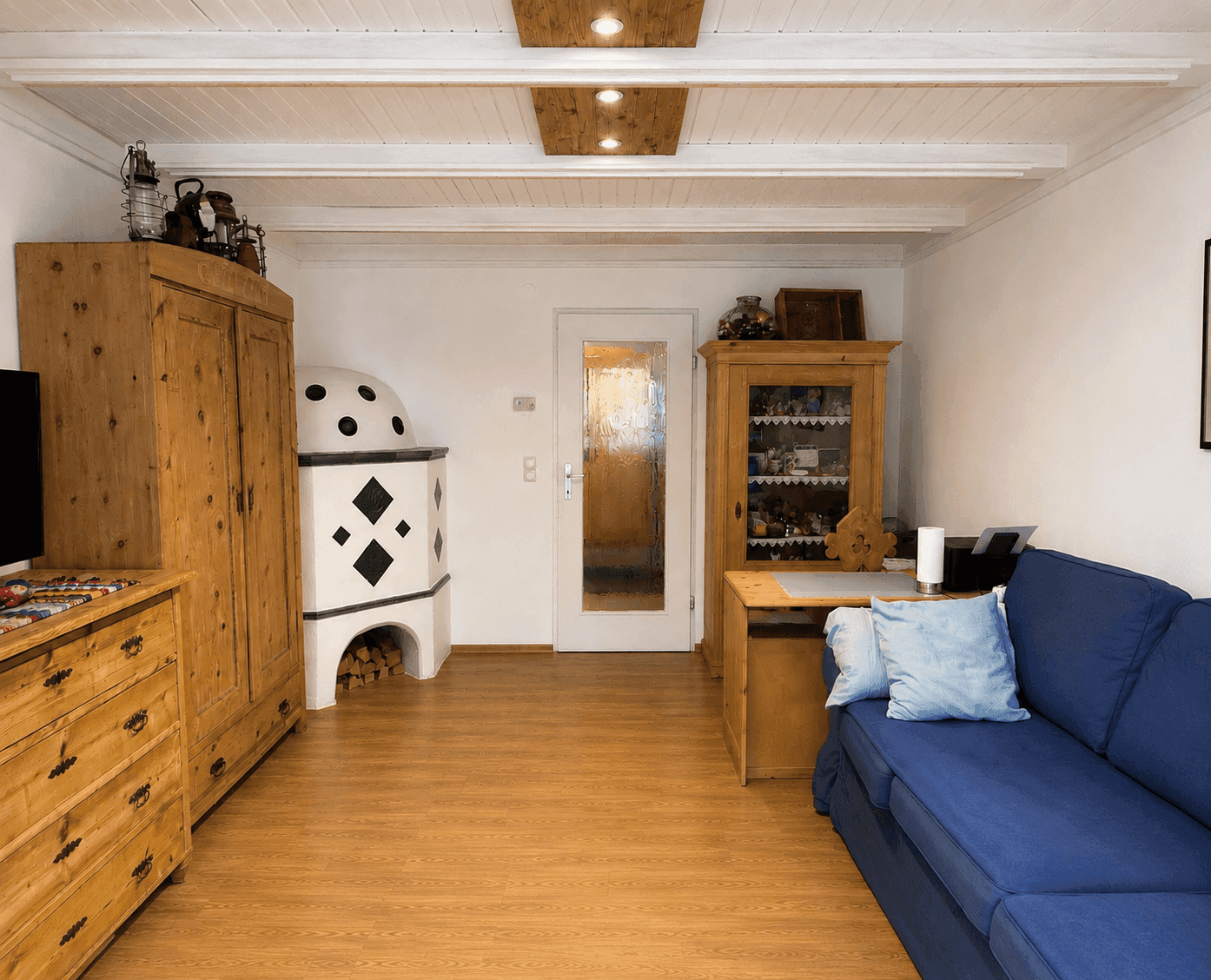 Gemütliches Wohnzimmer mit Kachelofen, blauem Sofa und traditionellen Holzmöbeln.