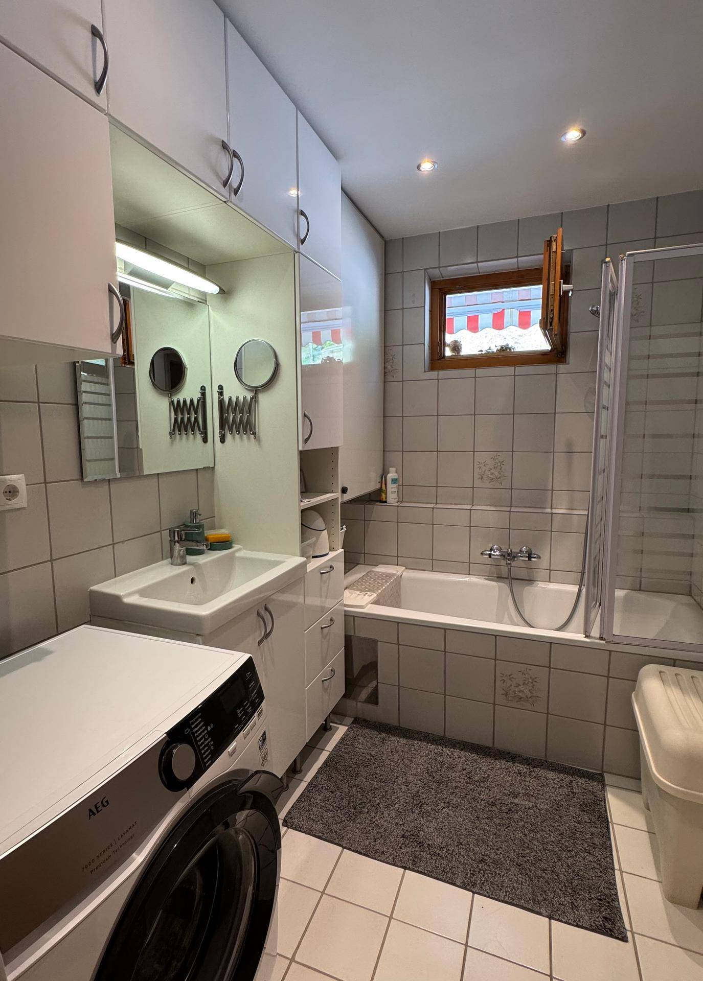 Funktionales Badezimmer mit Badewanne, Dusche, Waschbecken und Waschmaschine.