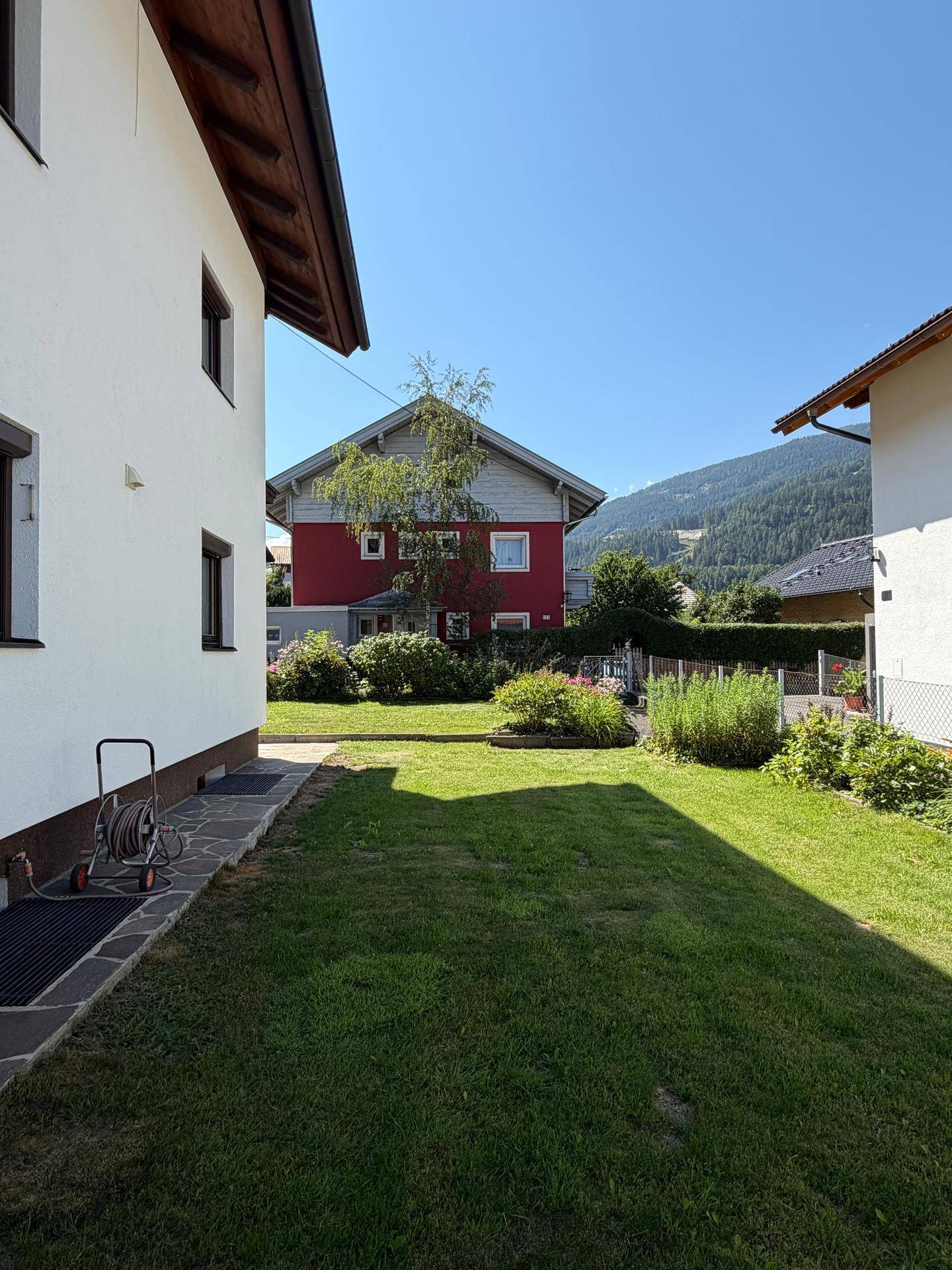 Großer grüner Gartenbereich neben dem Haus mit Blick auf die umliegenden Gebäude und Berge.