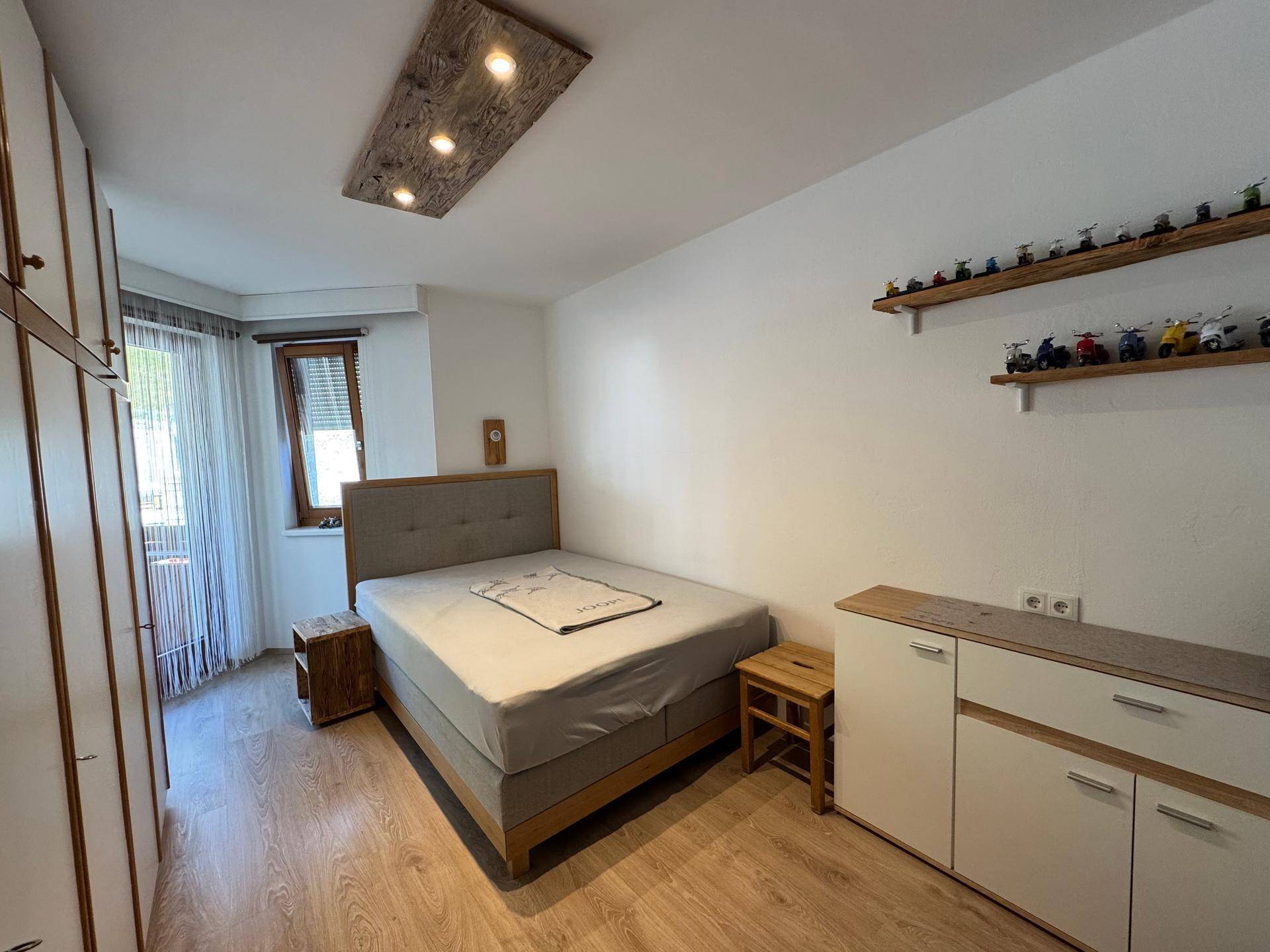 Helles Schlafzimmer mit Holzboden, Einbauschränken und einem Fenster mit Blick nach draußen.