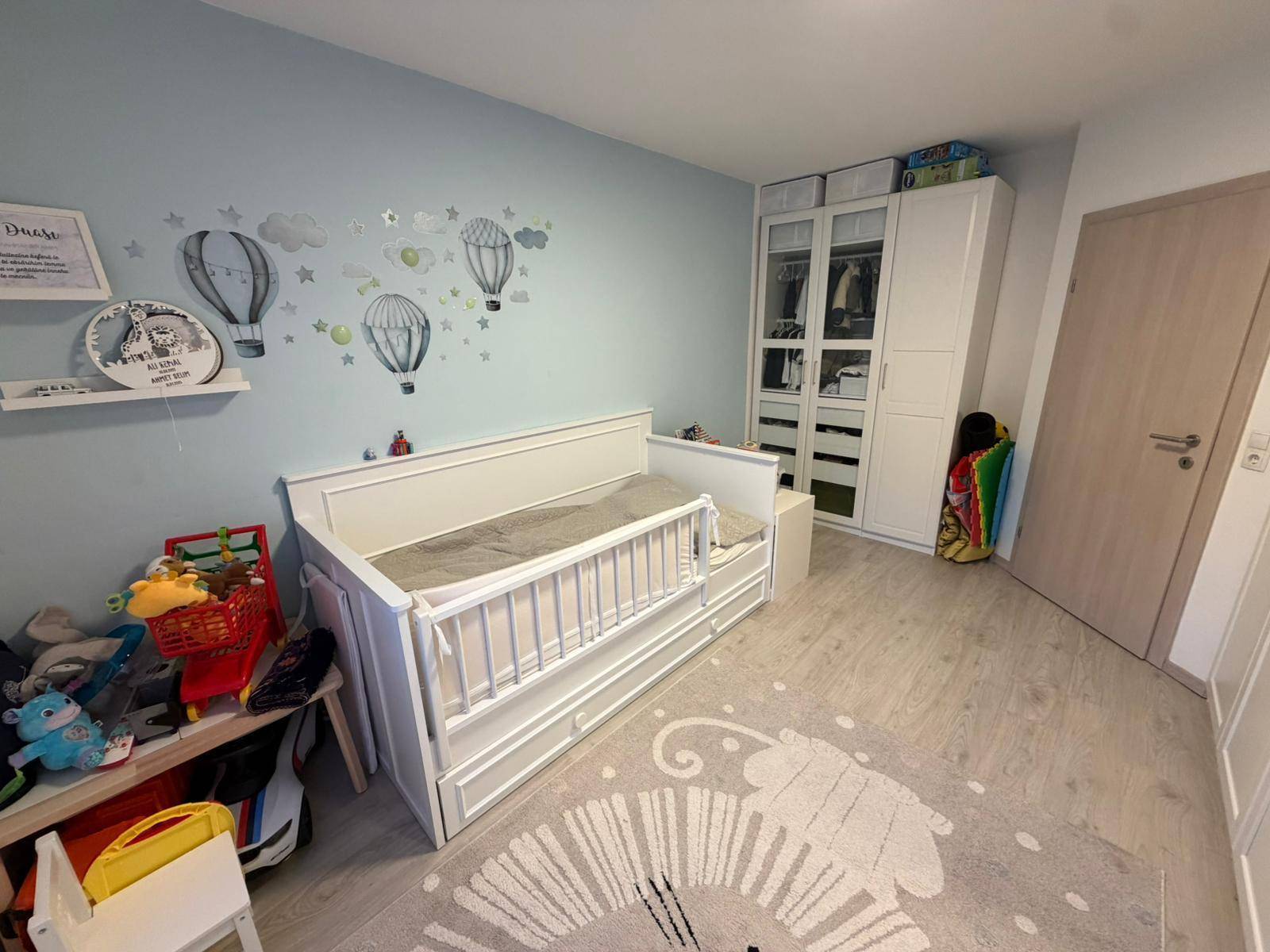 Helles Kinderzimmer mit weißem Bett, Kleiderschrank und verspielten Wanddekorationen.