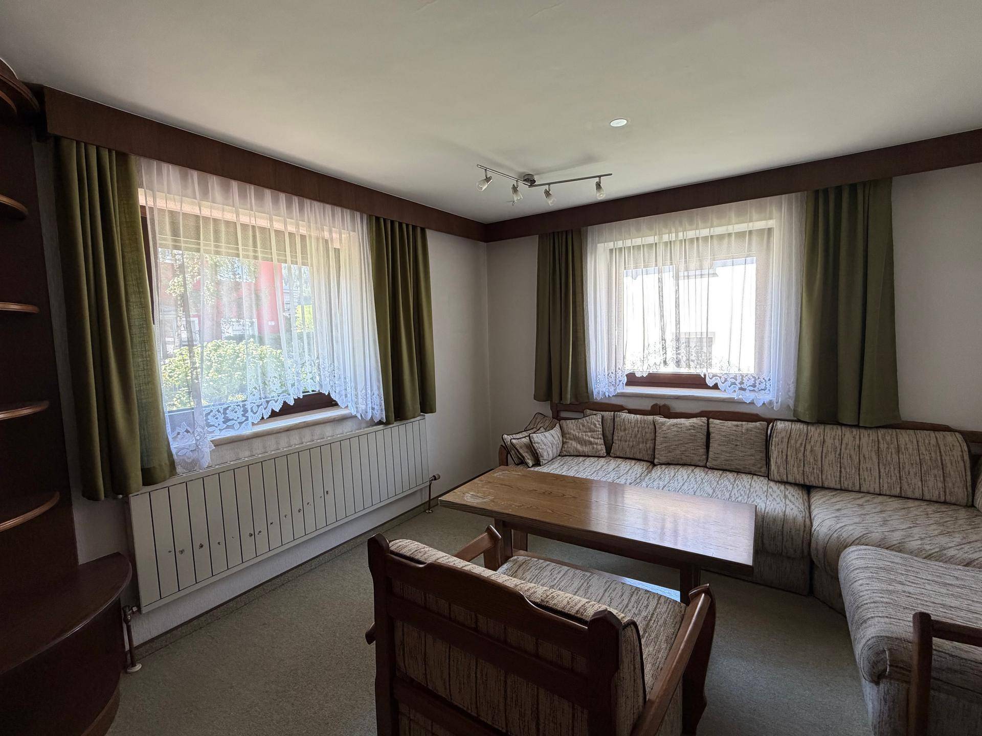 Gemütliches Wohnzimmer mit großem Sofa, Teppichboden und Fenstern mit grünen Vorhängen.