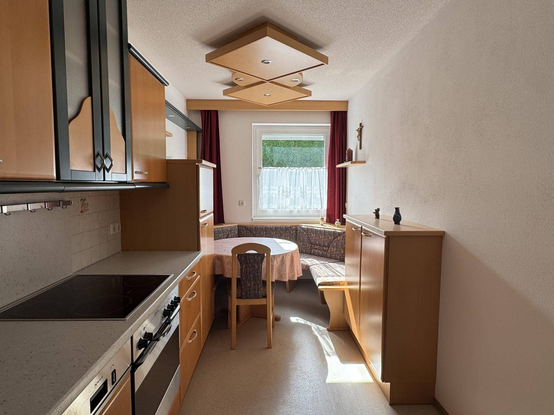 Gemütliche Wohnküche mit Holzeinbauten, Essecke und Fenster, das viel Licht hereinlässt.
