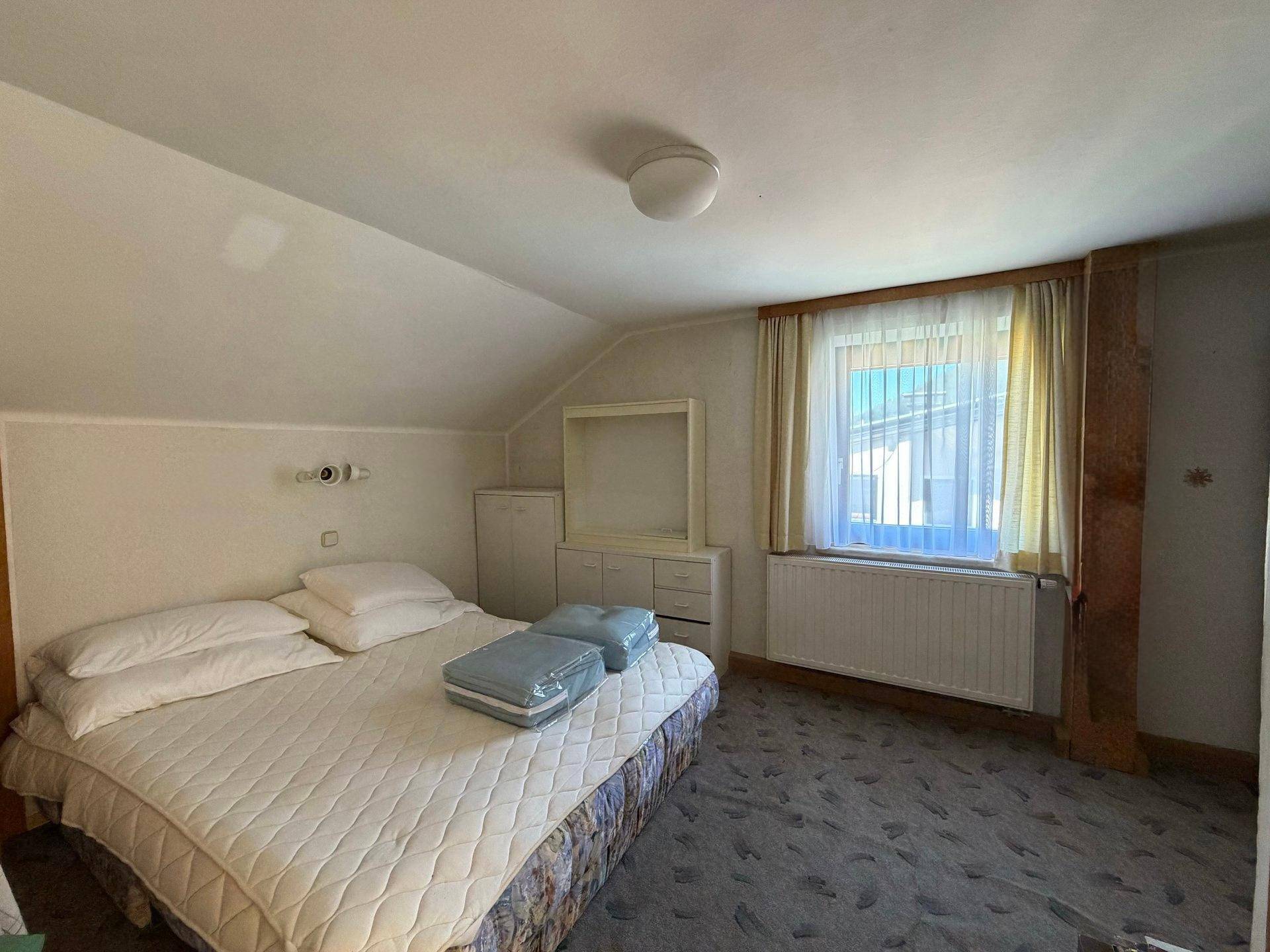 Schlafzimmer im Dachgeschoss mit Doppelbett, Teppichboden und einem Fenster mit Ausblick.