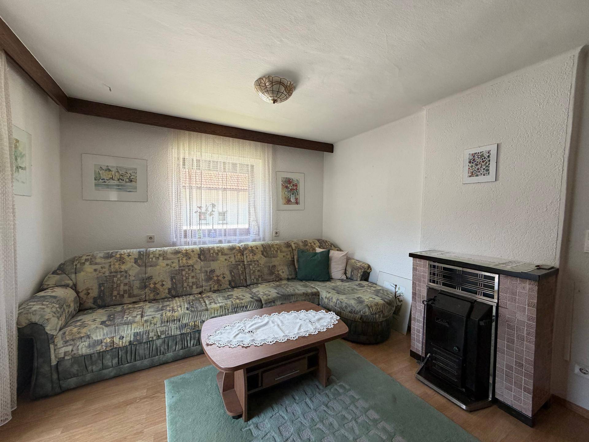 Gemütliches Wohnzimmer mit großem Sofa, Holzboden und einem traditionellen Kaminofen.
