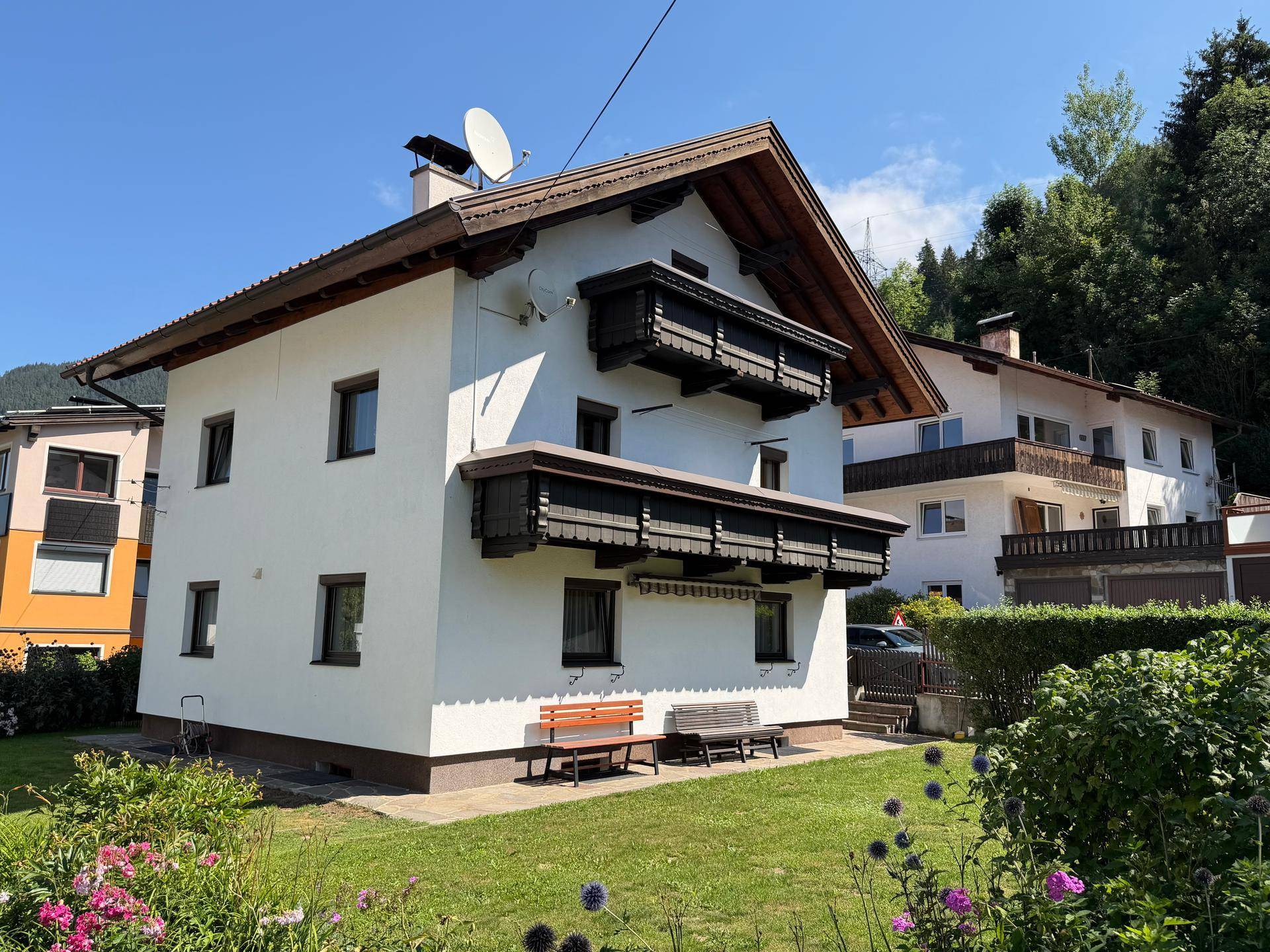 Traditionelles weißes Haus mit Holzbalkonen und Satteldach, umgeben von grüner Landschaft.