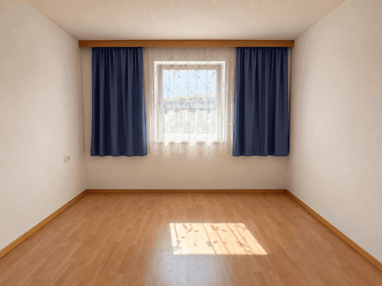 Gemütliches Schlafzimmer mit Holzboden und einem Fenster, das viel Tageslicht hereinlässt.
