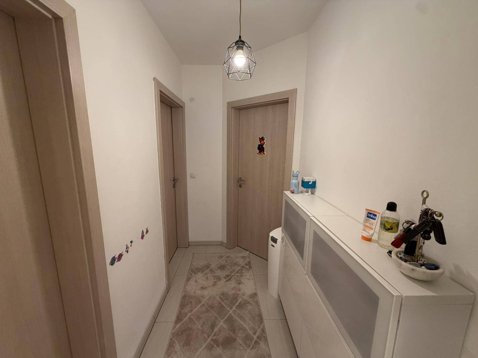 Heller Flur mit zwei Türen, einem kleinen Schrank und modernen Fliesen auf dem Boden.