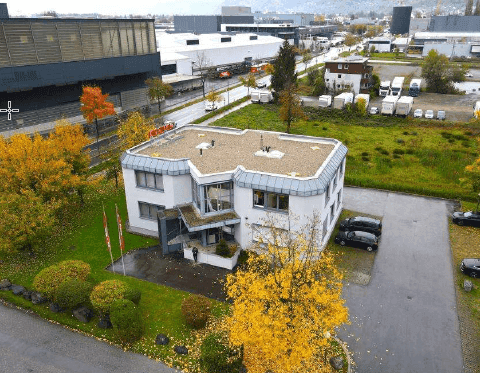 Luftaufnahme eines modernen Bürogebäudes mit Flachdach, umgeben von Bäumen und Parkplätzen.