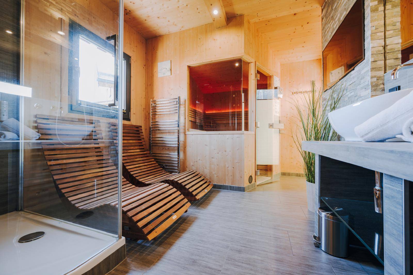 Moderner Wellnessbereich mit Holzvertäfelung, bequemen Liegen, Dusche und Sauna.