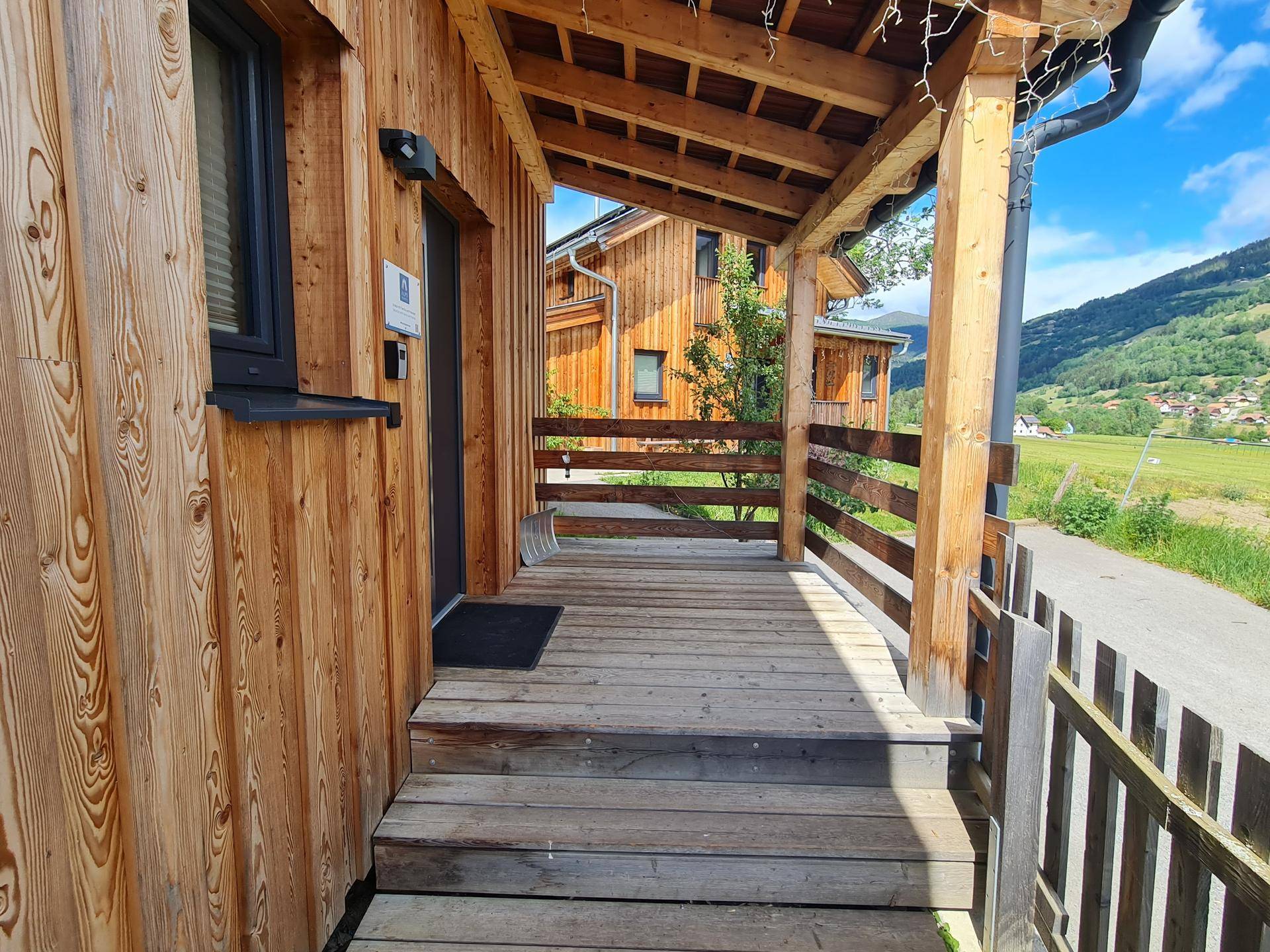 Überdachte Holzterrasse am Eingang eines Holzhauses mit Blick auf die Berge.