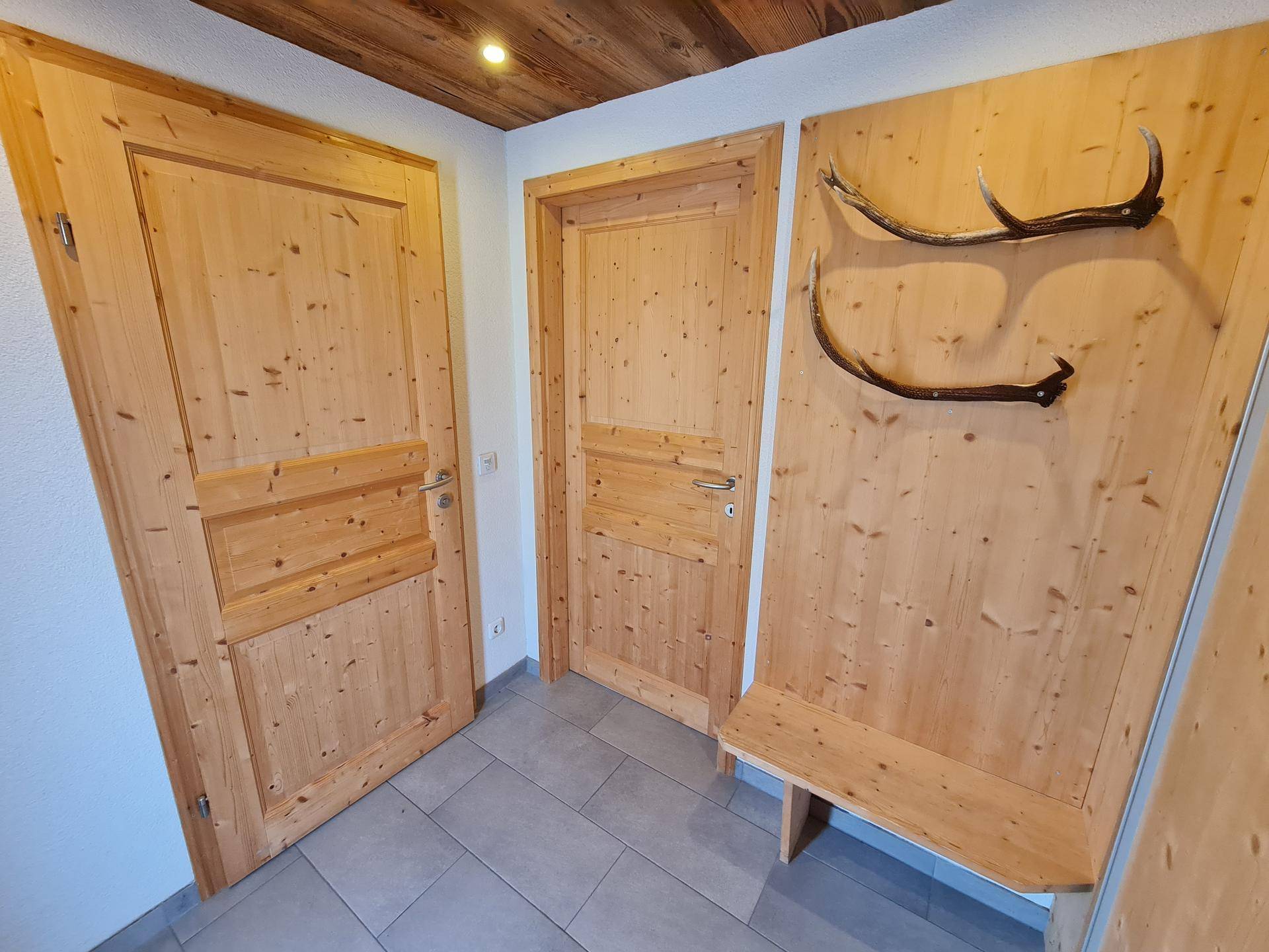 Eingangsbereich mit Holztüren, Fliesenboden und traditioneller Geweihdekoration an der Wand.