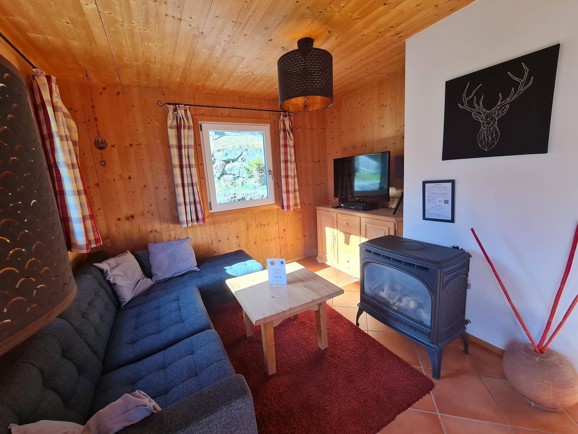 Gemütliches Wohnzimmer im alpinen Stil mit Kaminofen, Holzwänden und bequemer Couch.