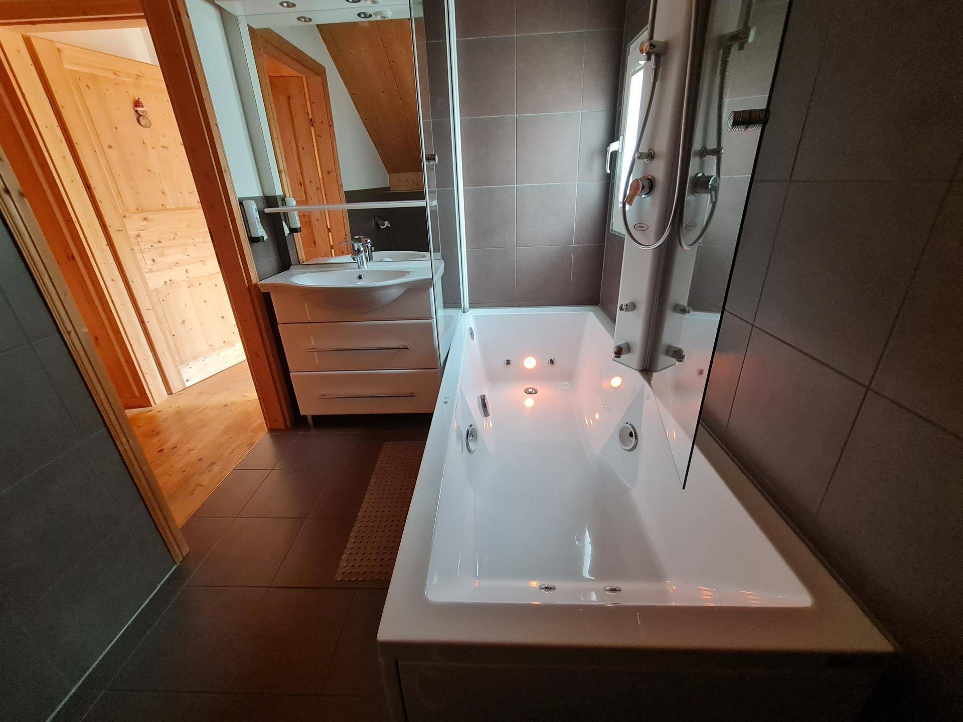 Modernes Badezimmer mit Badewanne, Waschbecken und dunklen Fliesen.