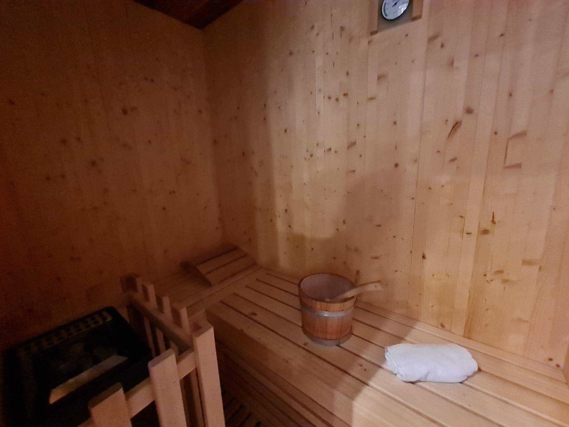 Gemütliche Holzsauna mit Bänken, Eimer und Sanduhr für entspannende Momente.