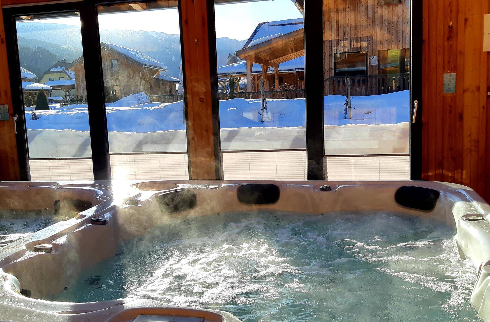 Warmer Whirlpool im Wellnessbereich mit Blick auf die verschneite Winterlandschaft.
