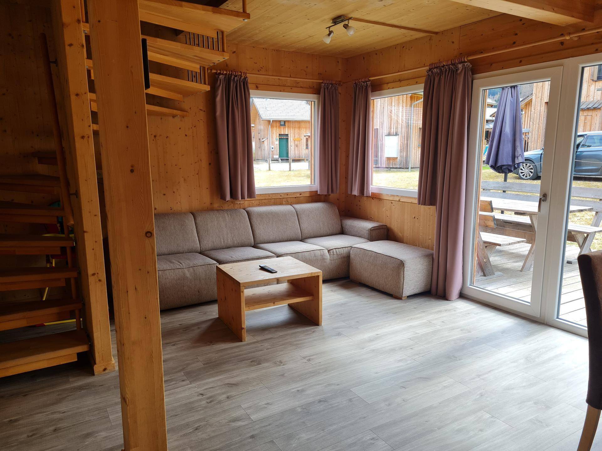 Gemütliches Wohnzimmer mit großem Sofa, Holzwänden und Blick ins Grüne.