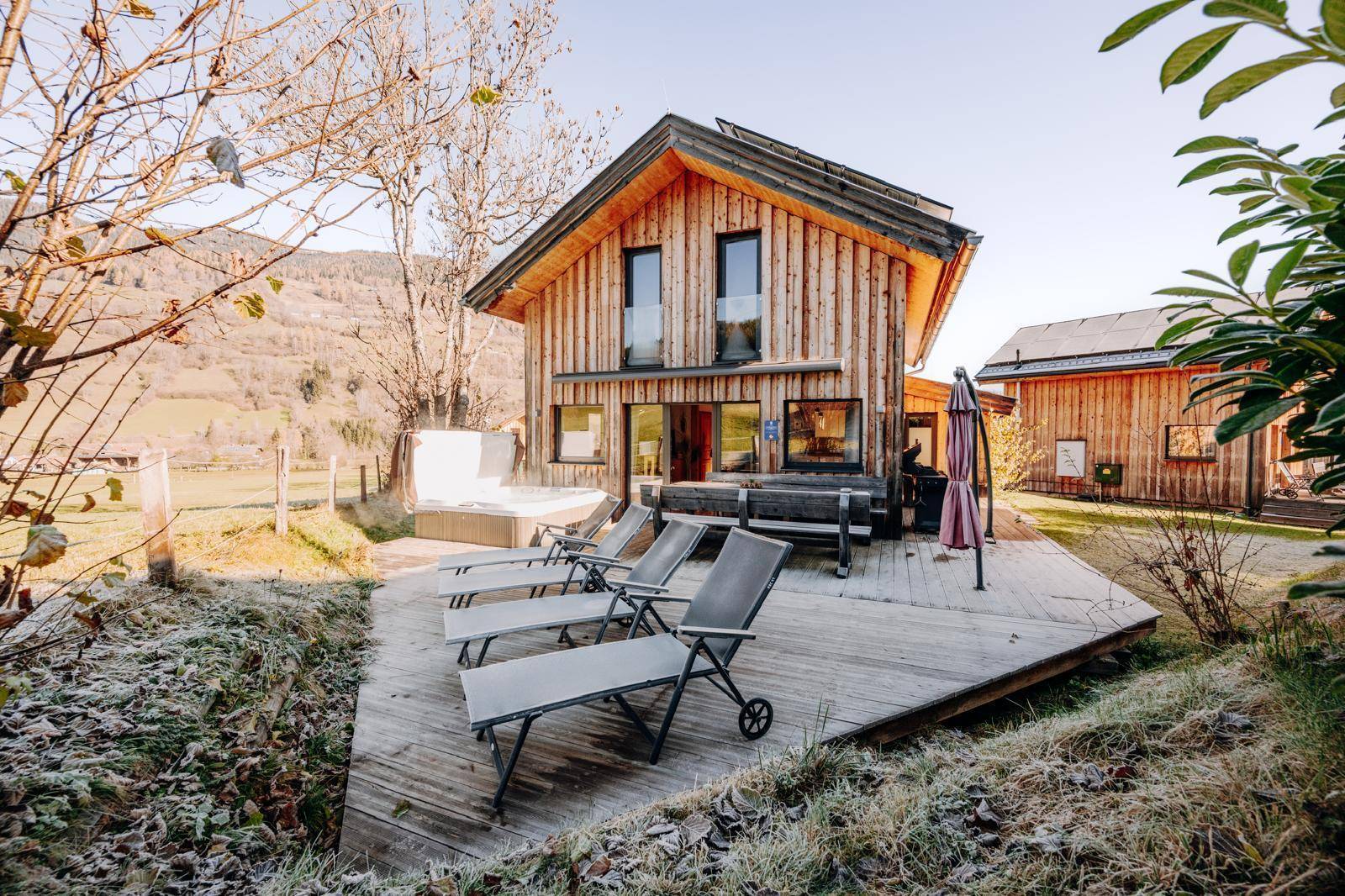 Holzhaus mit großer Holzterrasse, Sonnenliegen und einem Whirlpool im Freien.