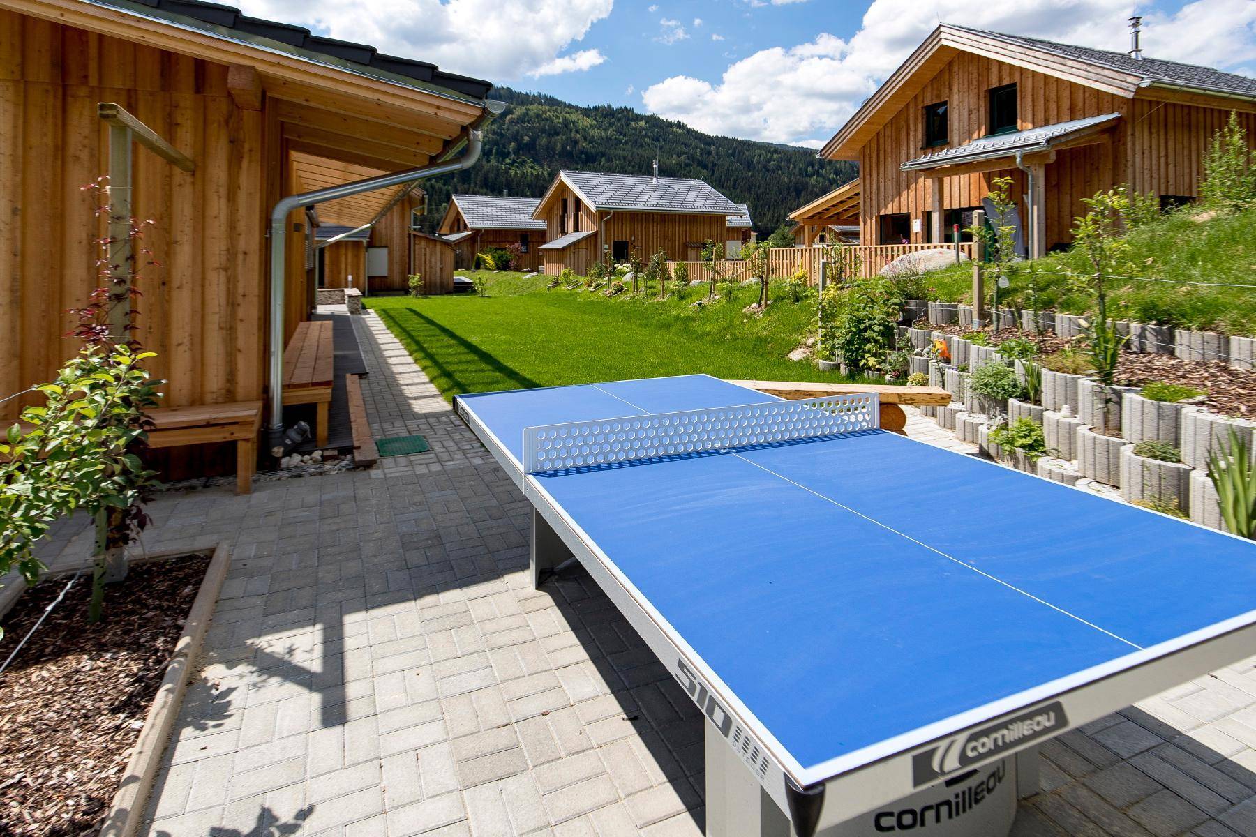 Außenbereich mit Tischtennisplatte und gepflegtem Rasen zwischen den Holzhäusern.