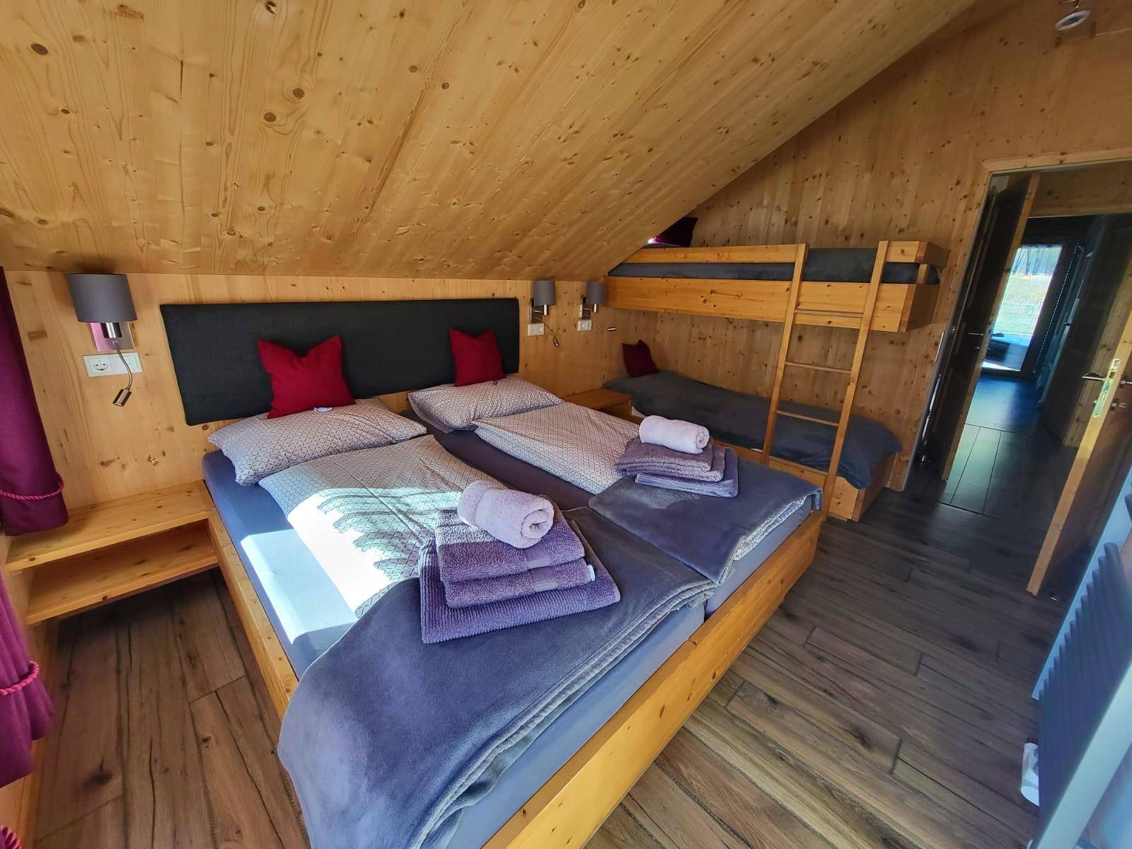 Gemütliches Schlafzimmer im Dachgeschoss mit Holzwänden, Doppelbett und Etagenbett.