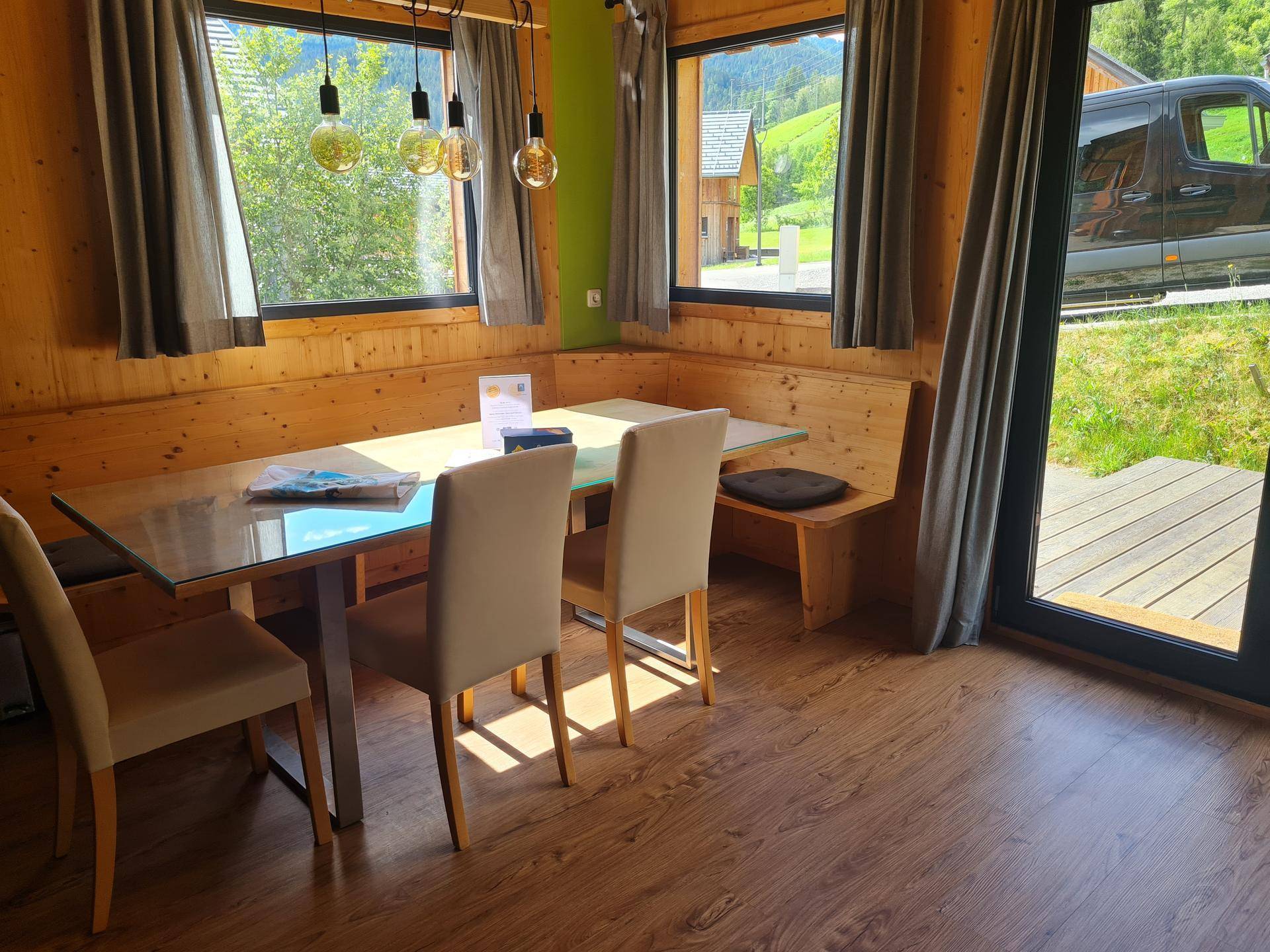 Gemütlicher Essbereich mit Holzwänden, großem Tisch und Blick ins Grüne durch die Fenster.